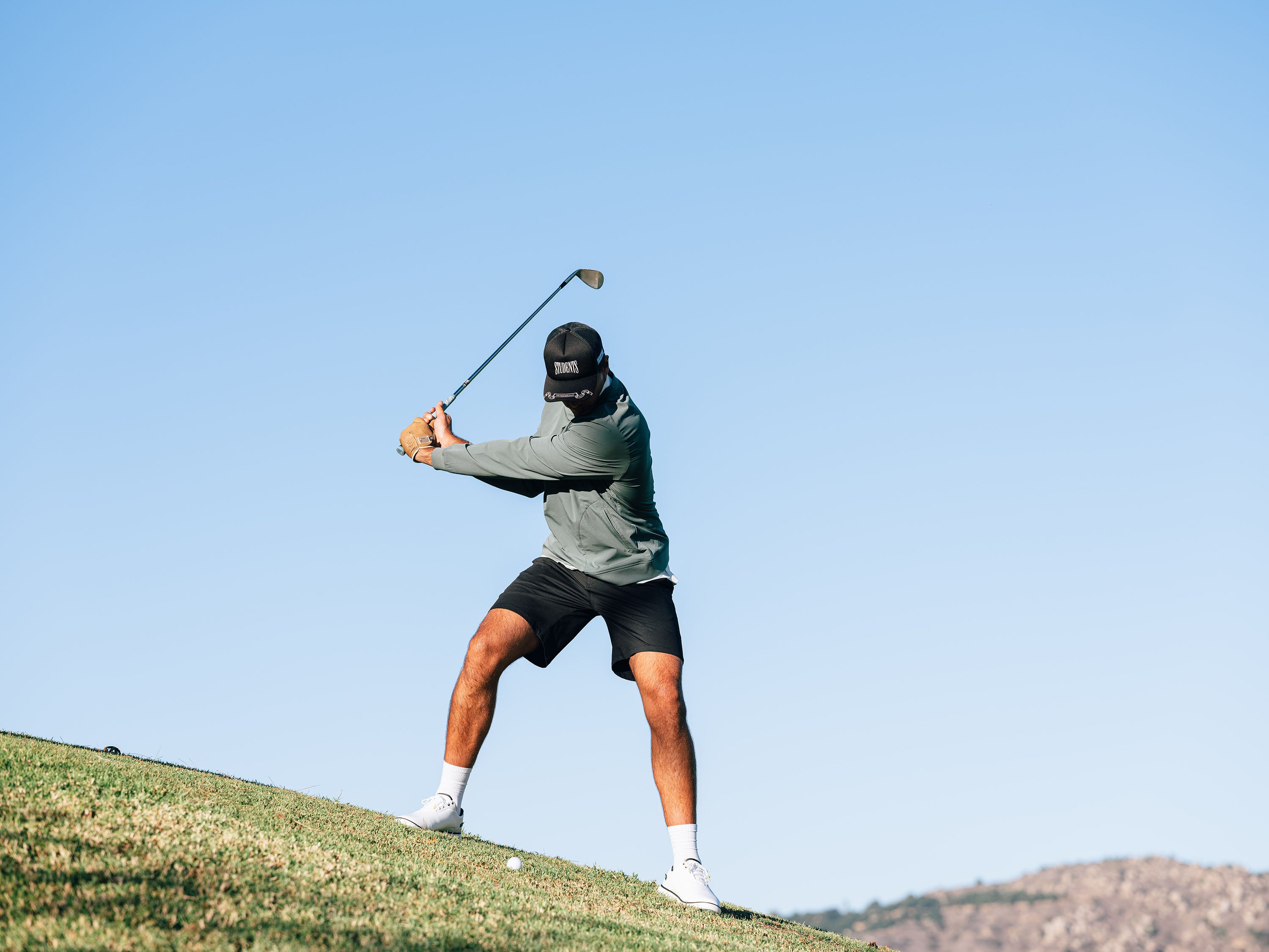Person playing golf on a clear day with mountains in the background