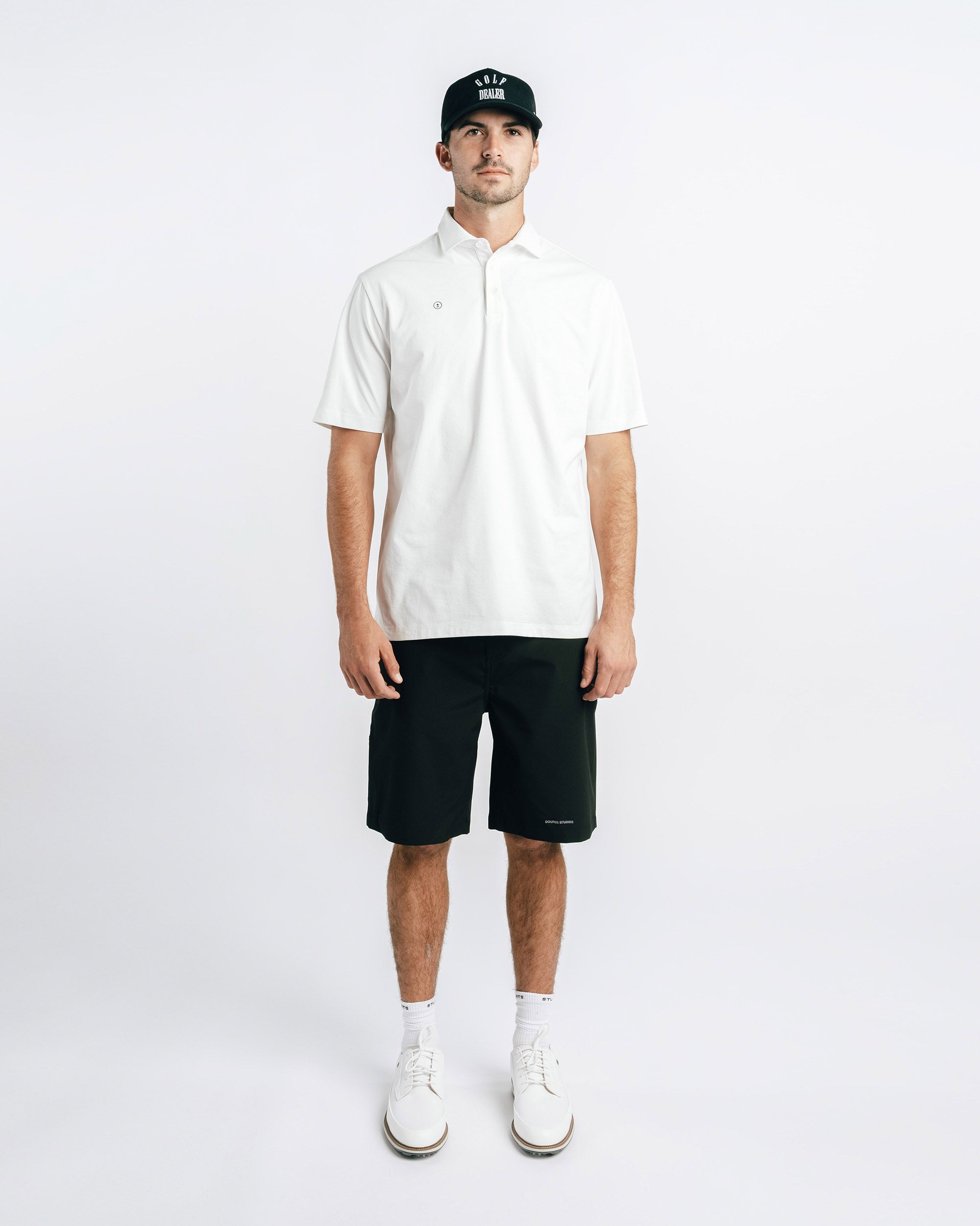 Man wearing a white polo shirt, black shorts, and a black cap on a white background