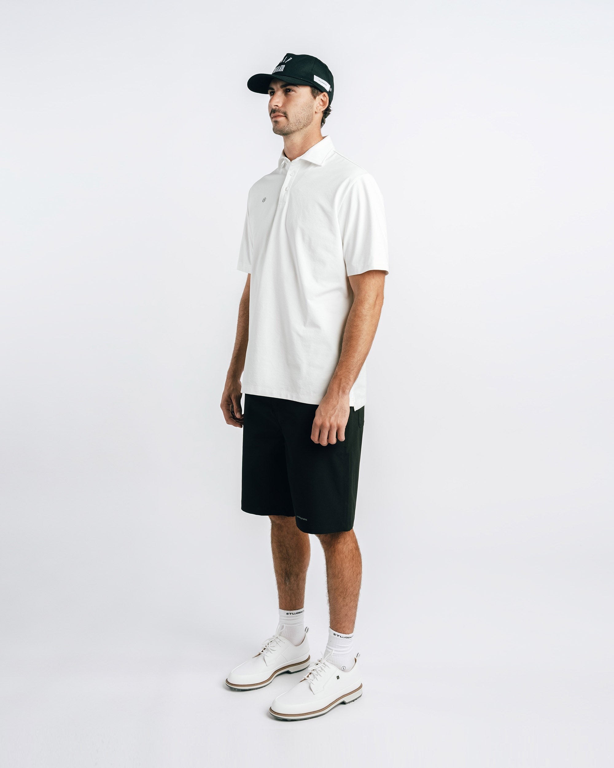 Man wearing a white polo shirt, black shorts, and a cap on a white background