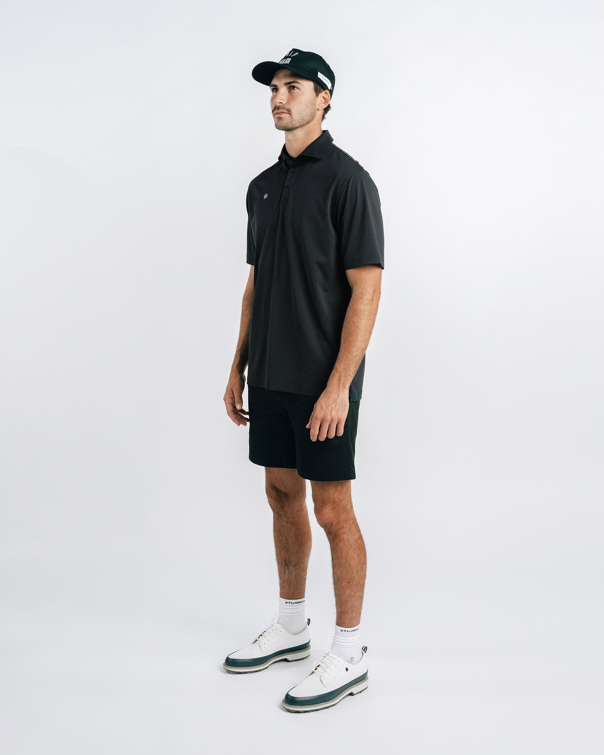 Man wearing a black polo shirt and shorts with a cap on a white background