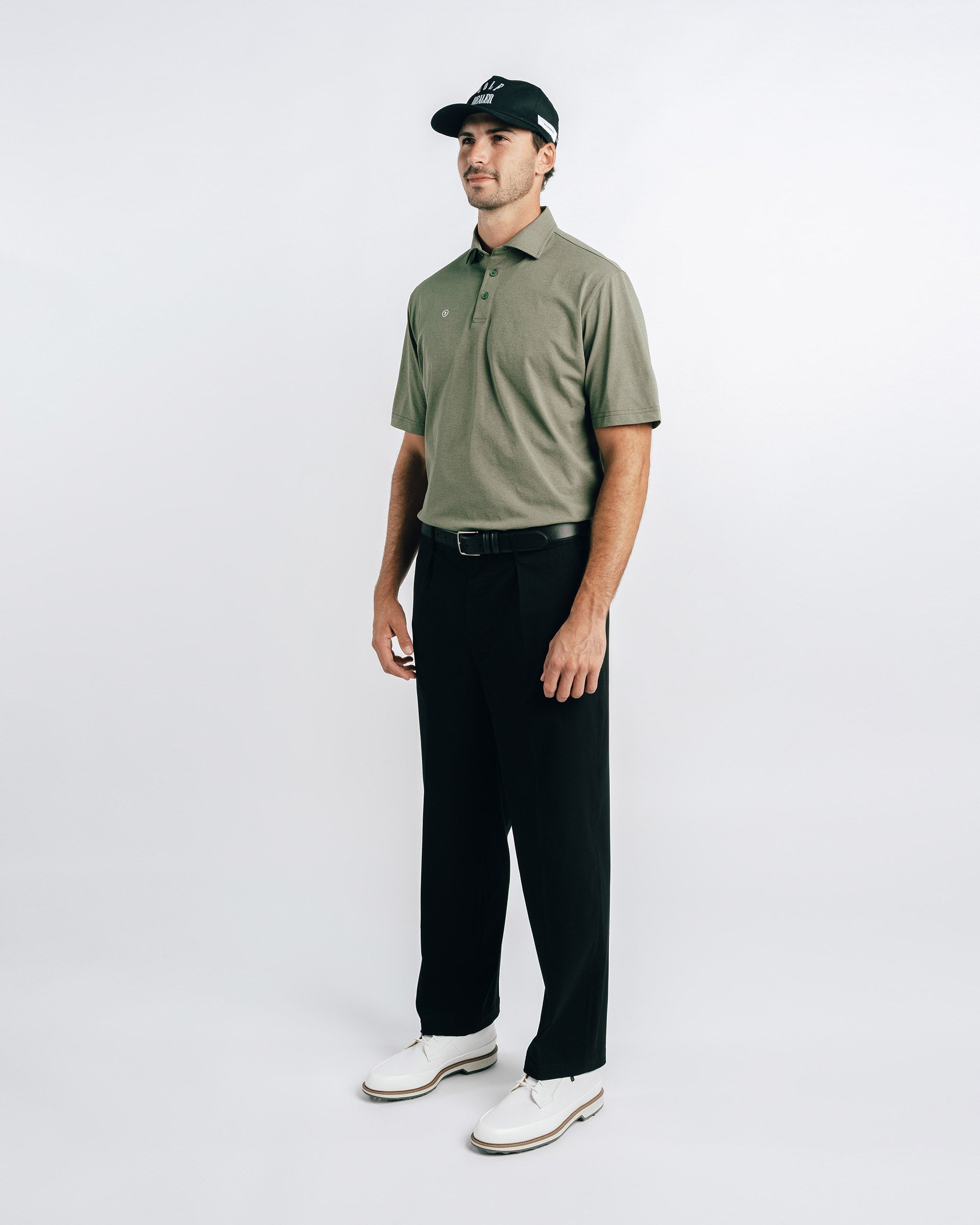 Man wearing a green polo shirt, black pants, and white shoes on a white background