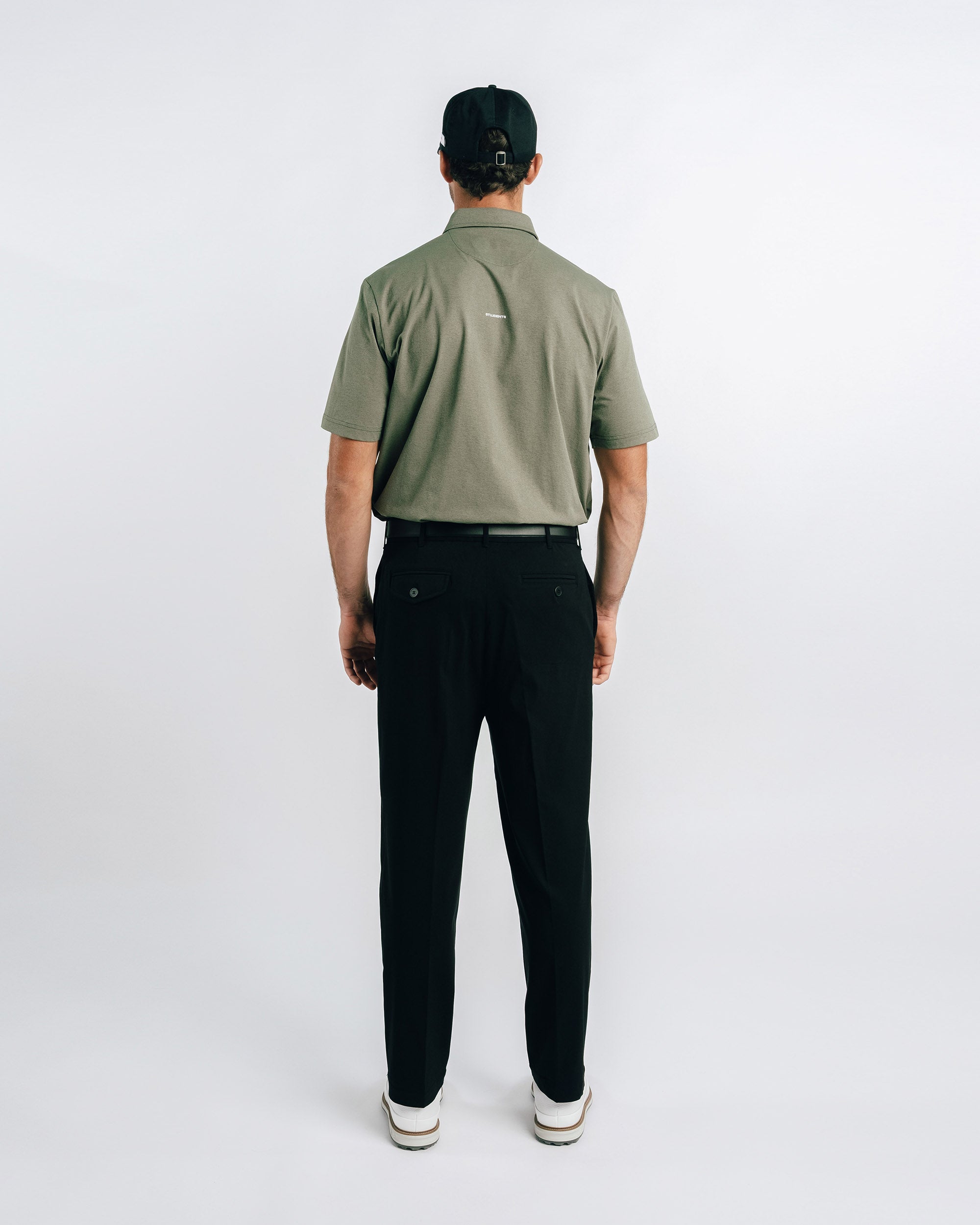 Person wearing a green polo shirt and black pants on a white background