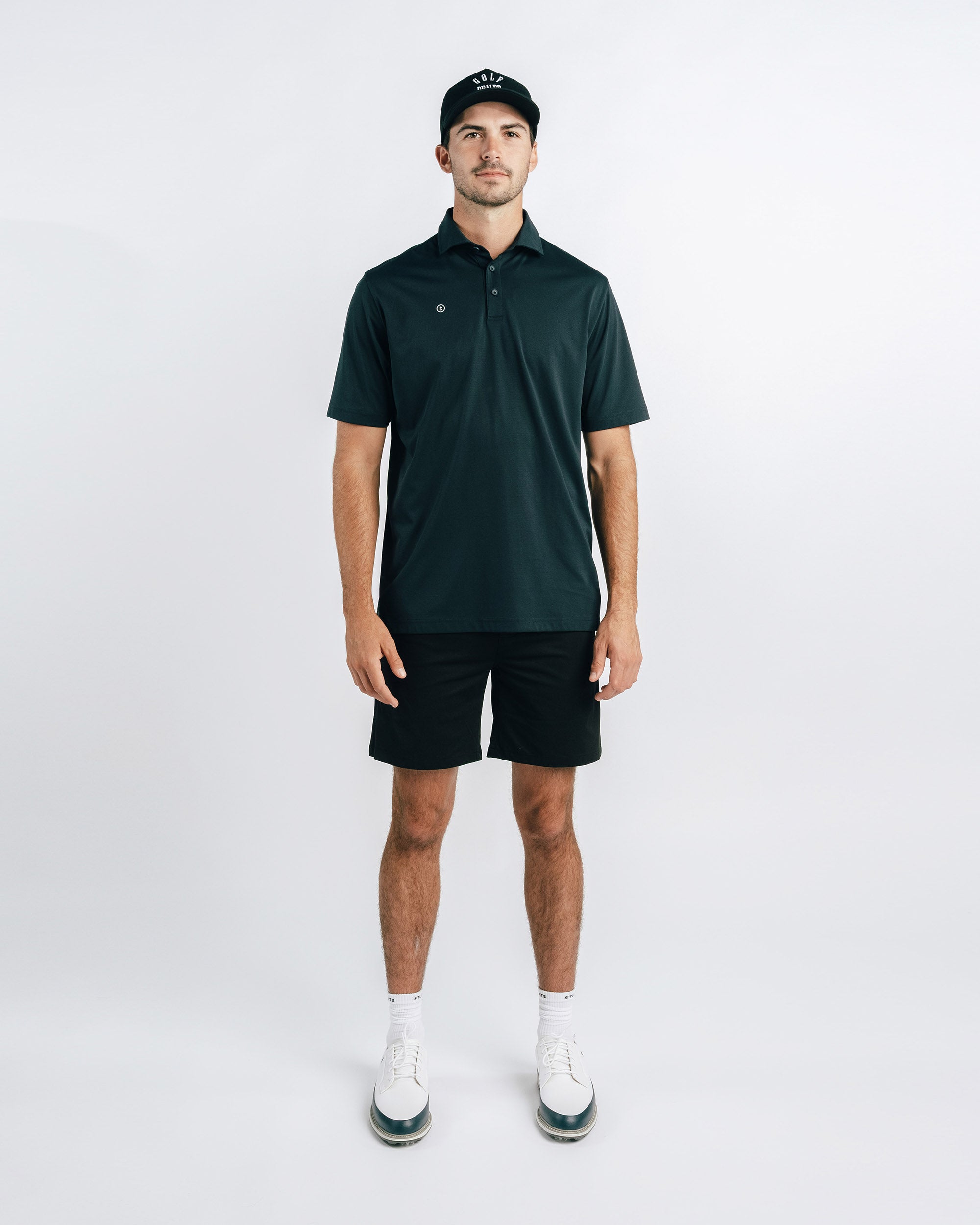 Man wearing a dark green polo shirt and black shorts on a white background