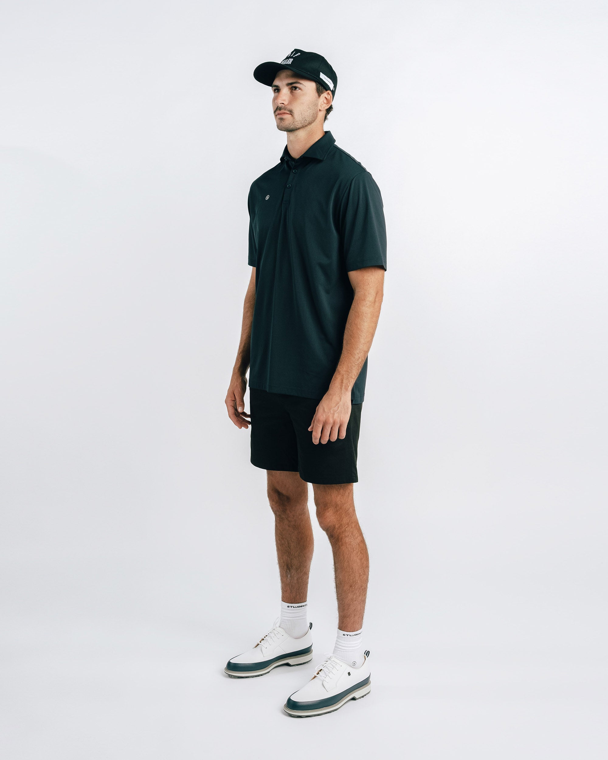 Man wearing a dark green polo shirt and black shorts on a white background