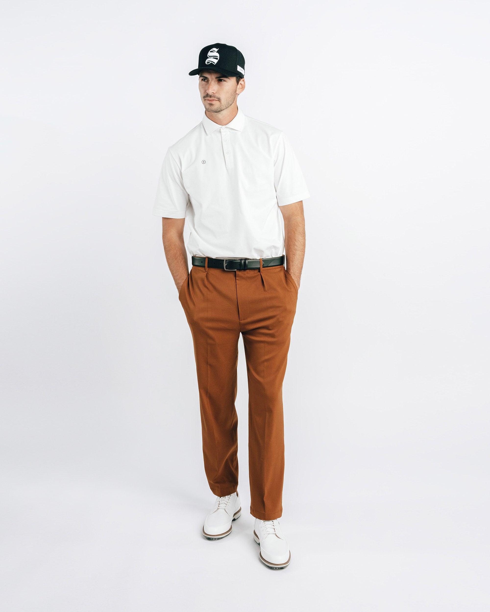 Man wearing a white polo shirt, brown pants, and a black cap on a white background