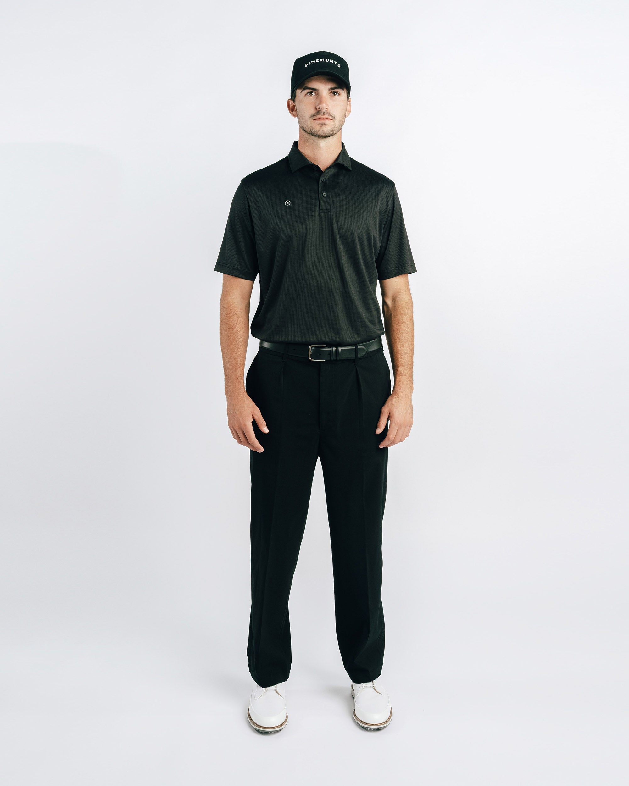 Man wearing a black golf outfit with a cap on a white background