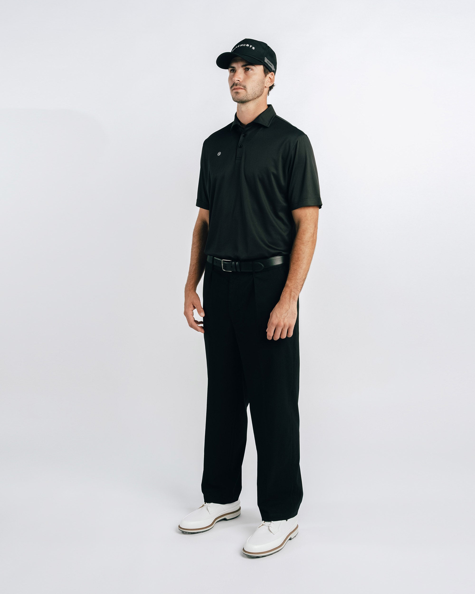 Man wearing a black polo shirt, black pants, and white shoes on a white background