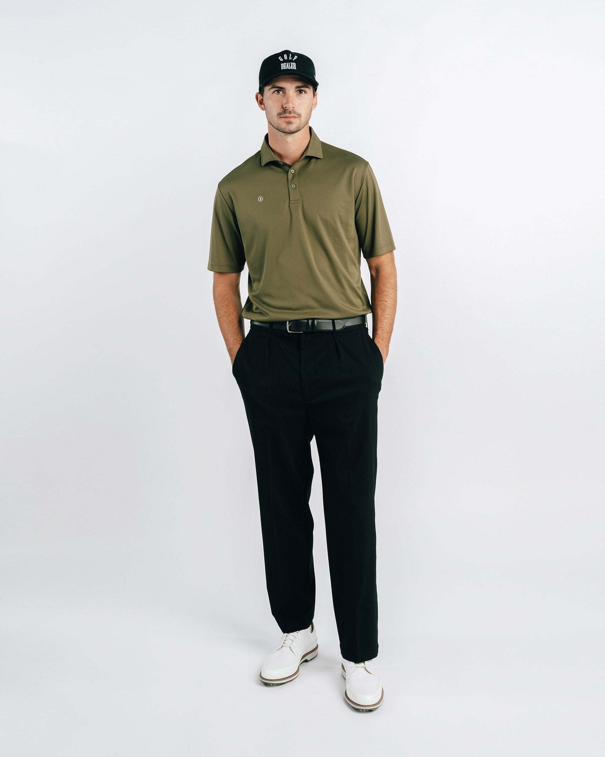 Man wearing a green polo shirt, black pants, and white shoes on a white background