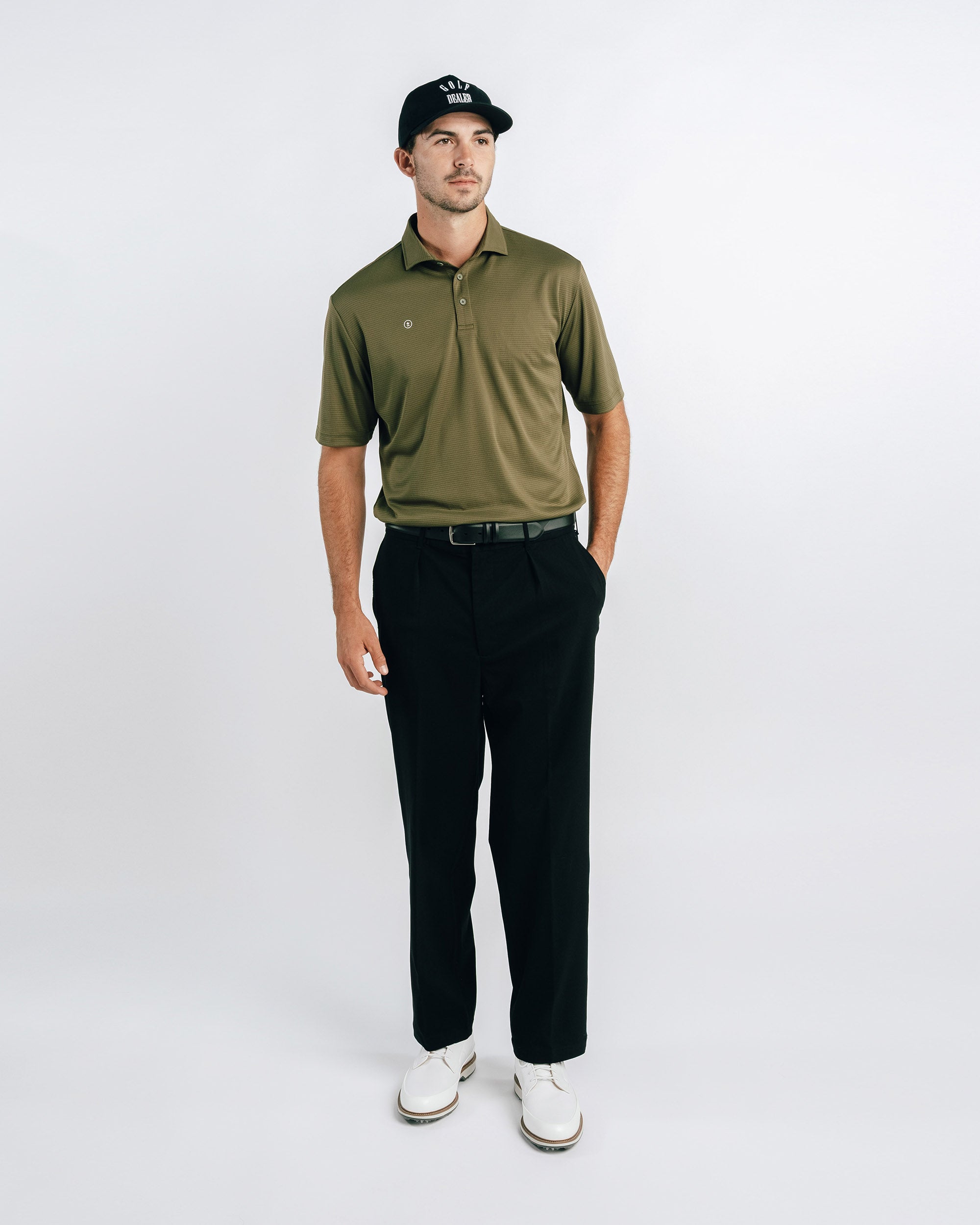 Man wearing a green polo shirt, black pants, and a cap on a white background