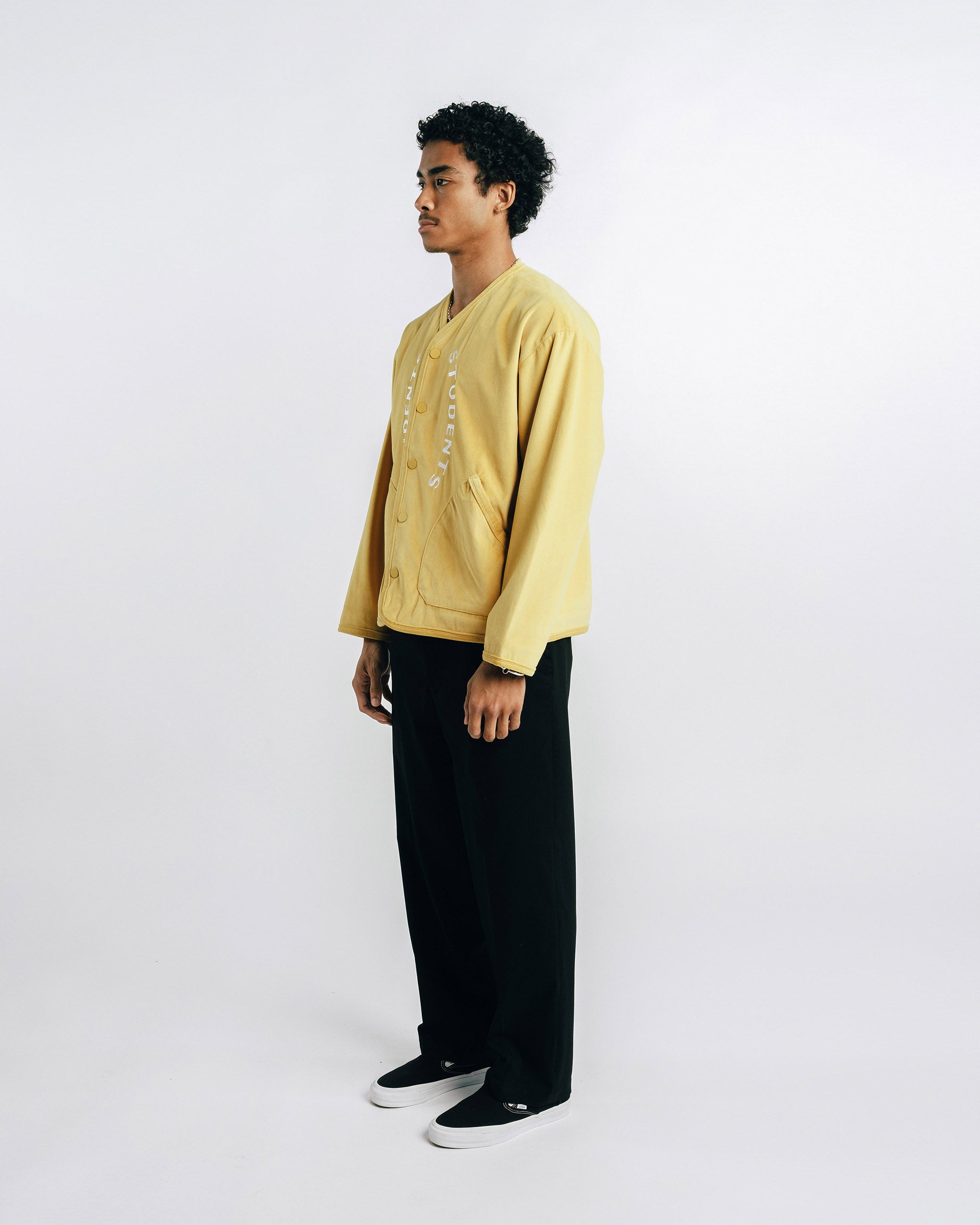Person wearing a yellow jacket and black pants on a white background