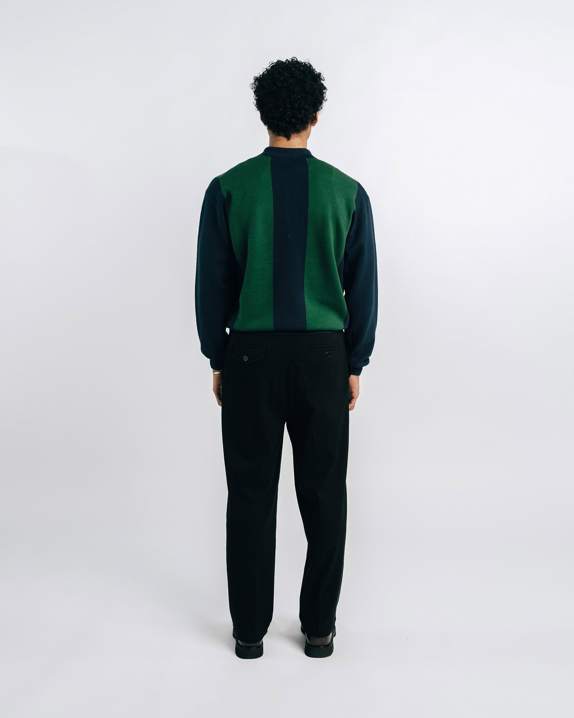 Man wearing a green and black shirt with black pants on a white