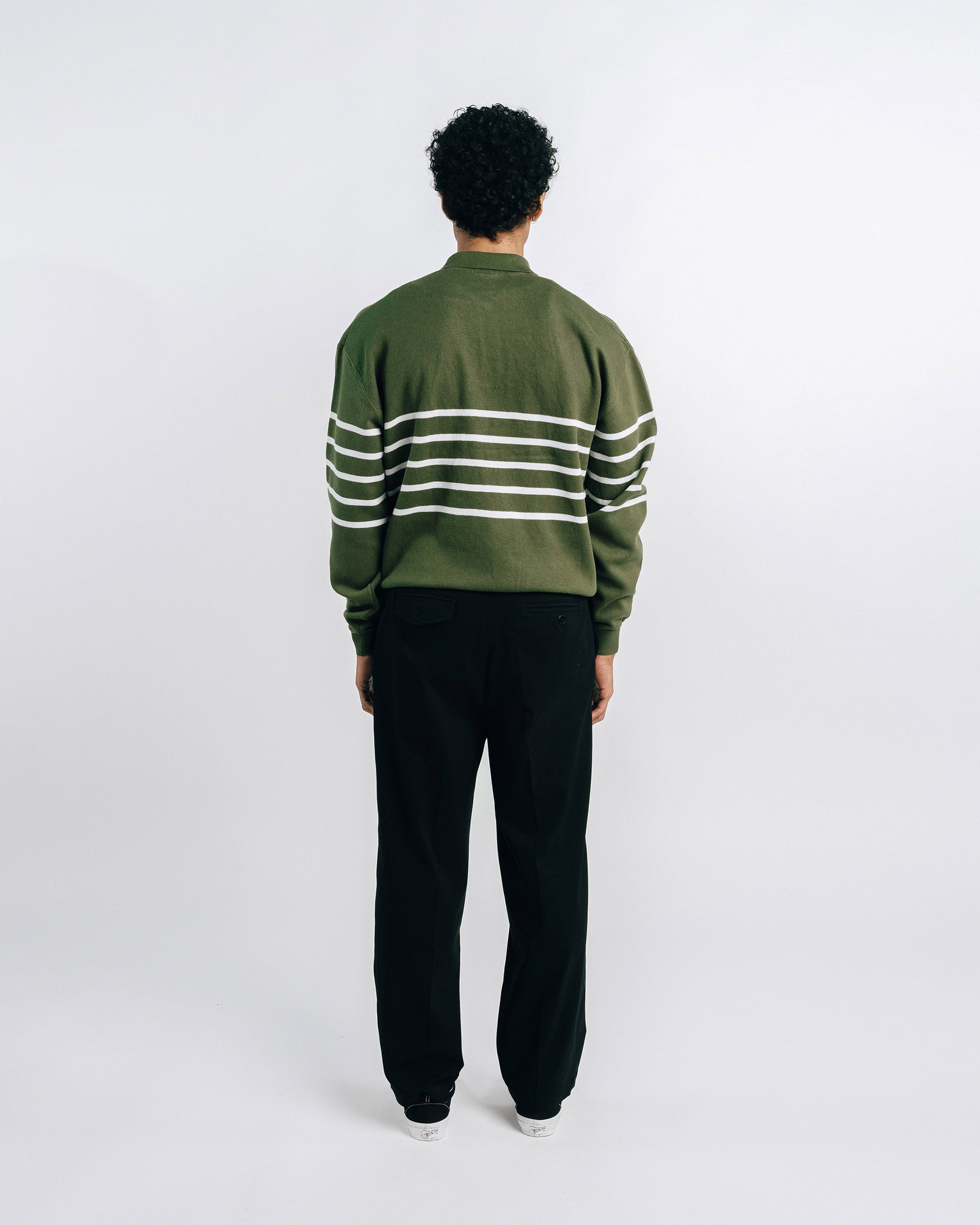 Person wearing a green and white striped sweater with black pants on a white background