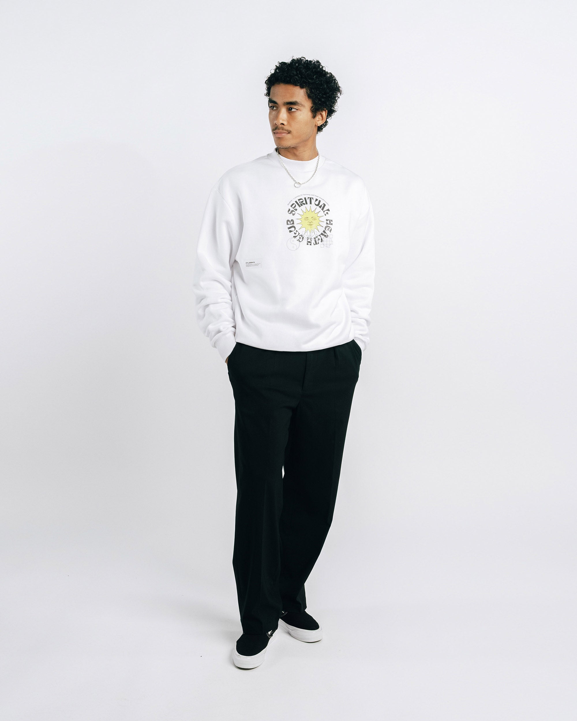 Person wearing a white sweatshirt with a logo and black pants on a white background