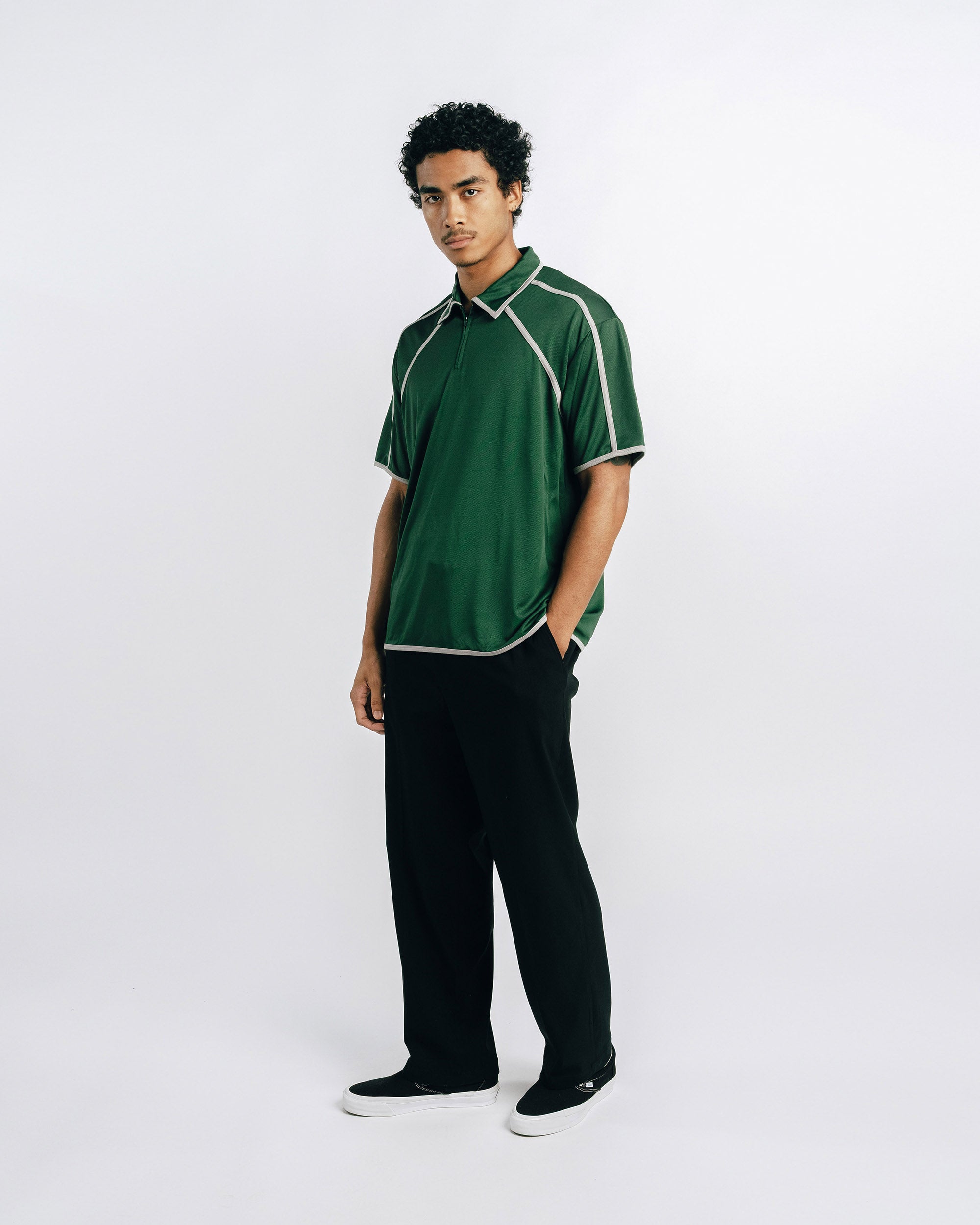 Person wearing a green polo shirt and black pants on a white background