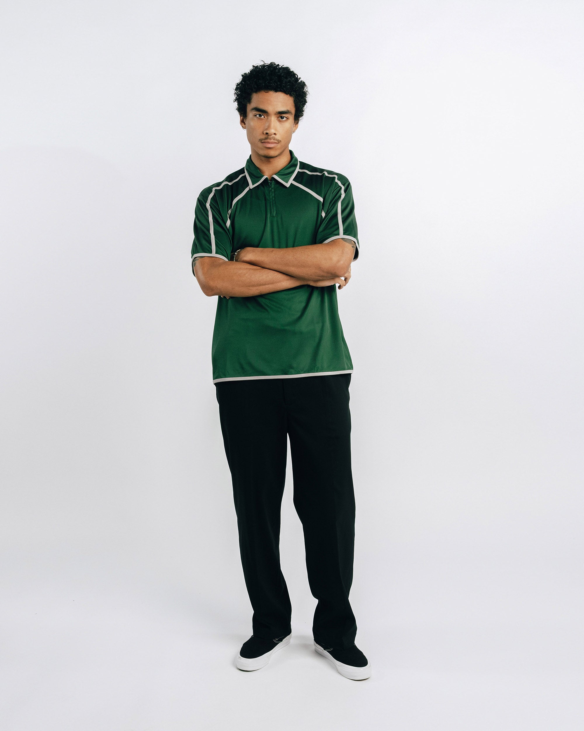 Person wearing a green polo shirt and black pants on a white background
