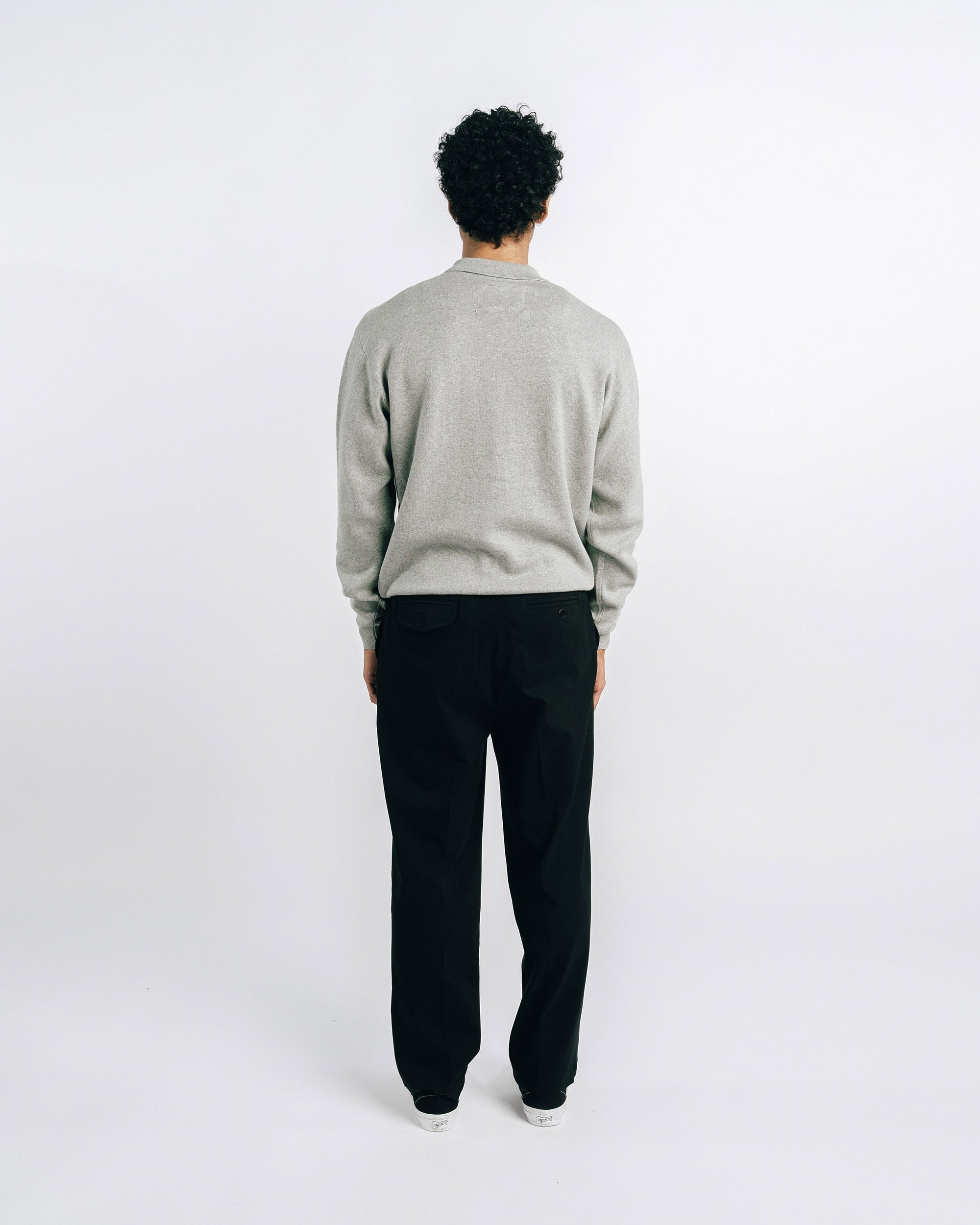 Person wearing a gray sweater and black pants on a white background