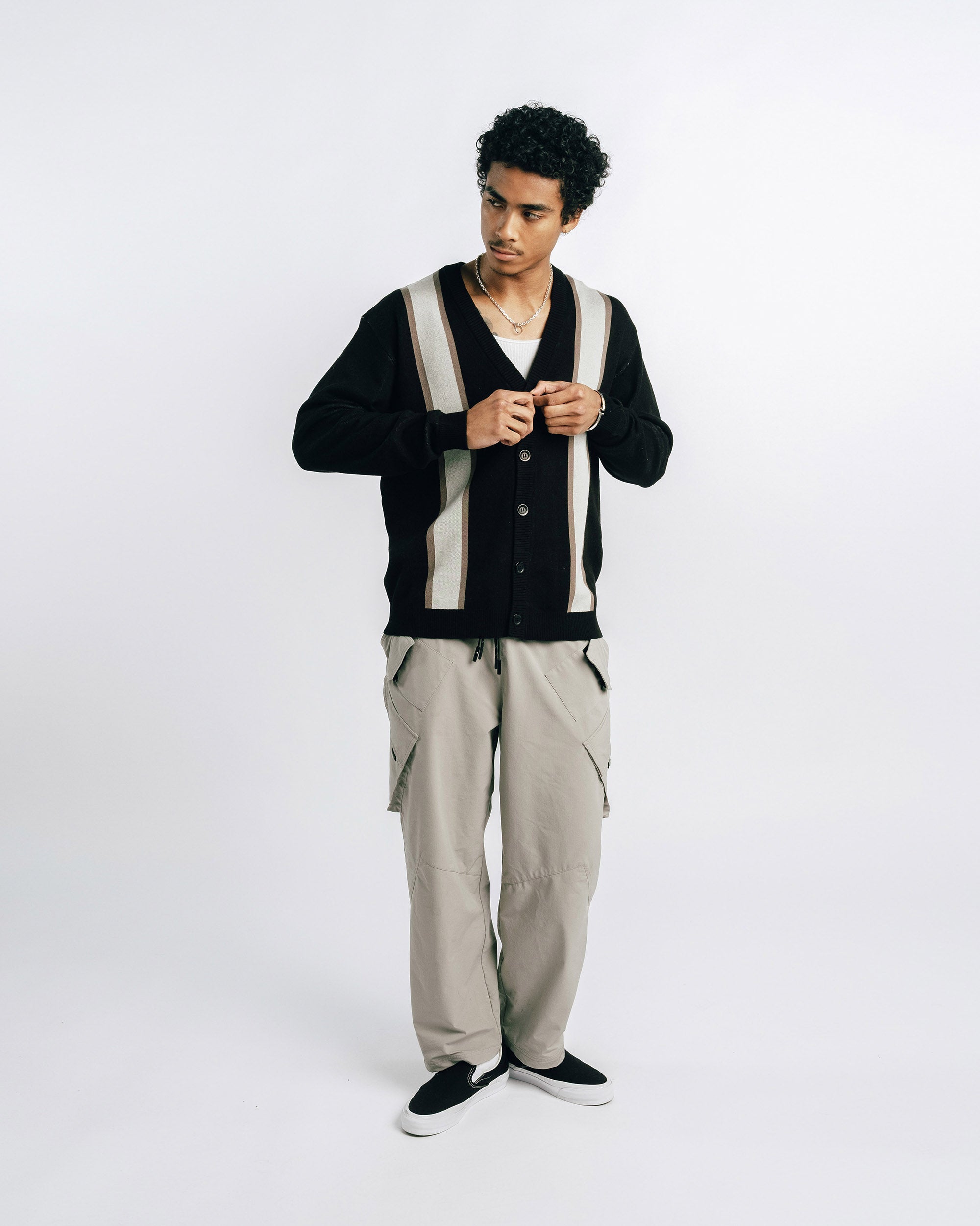 Person wearing a black and white striped cardigan with beige pants on a white background