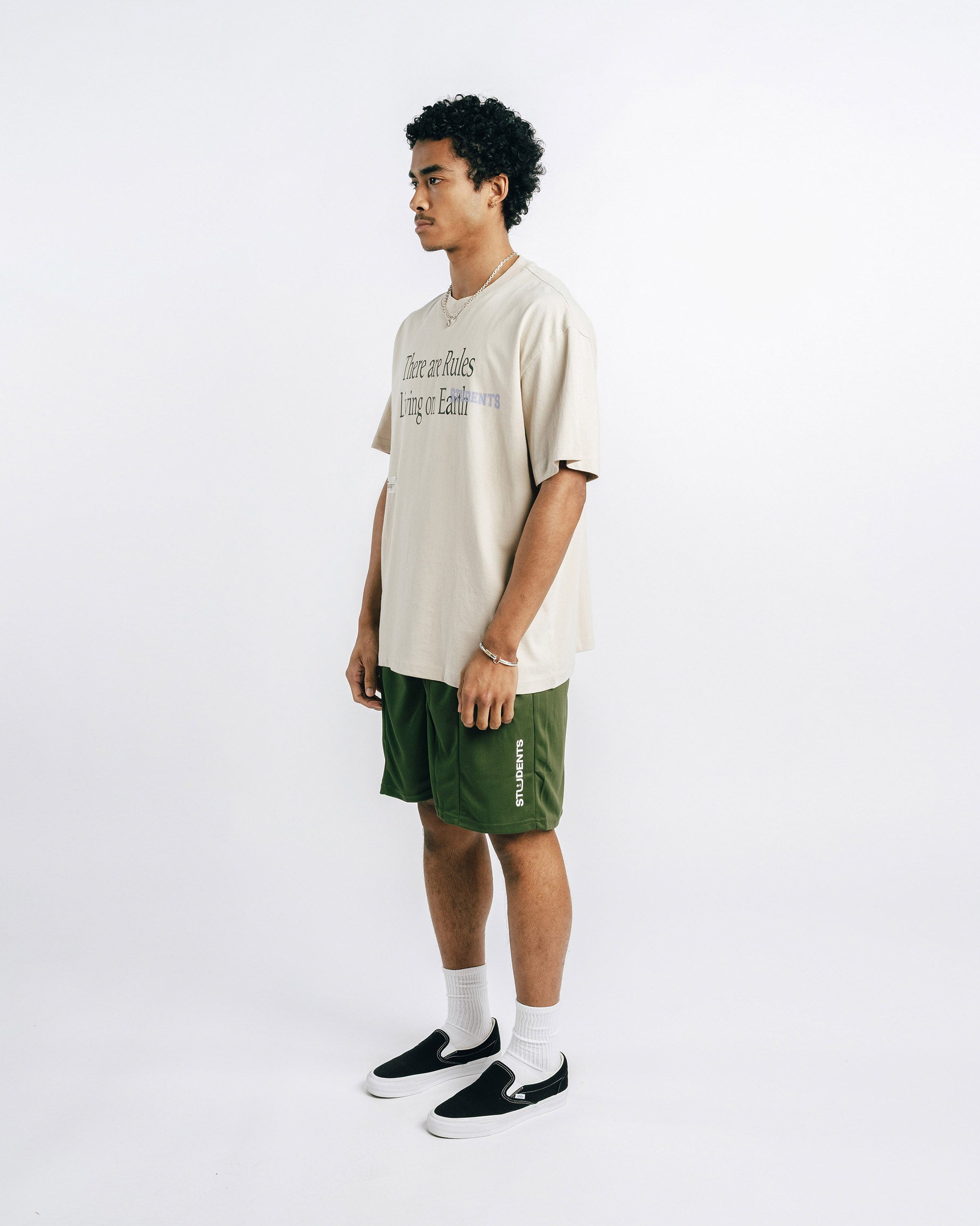 Man wearing a beige t-shirt and green shorts on a white background