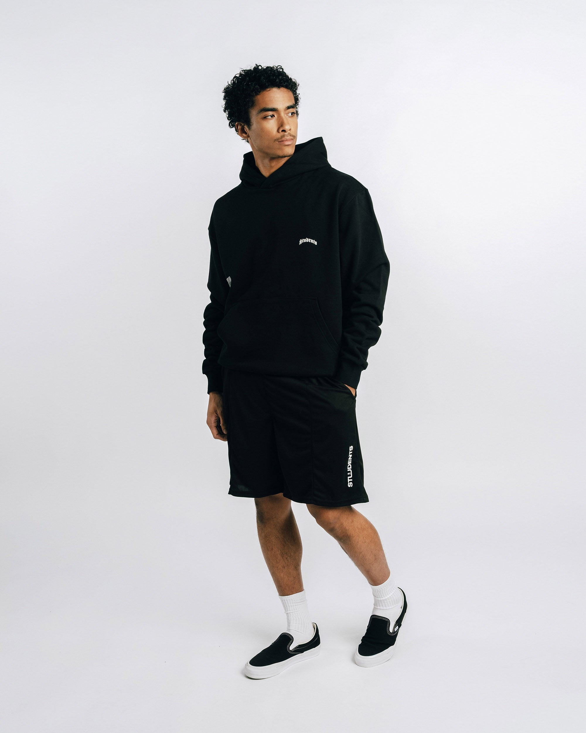 Person wearing a black hoodie and shorts with a logo on a white background
