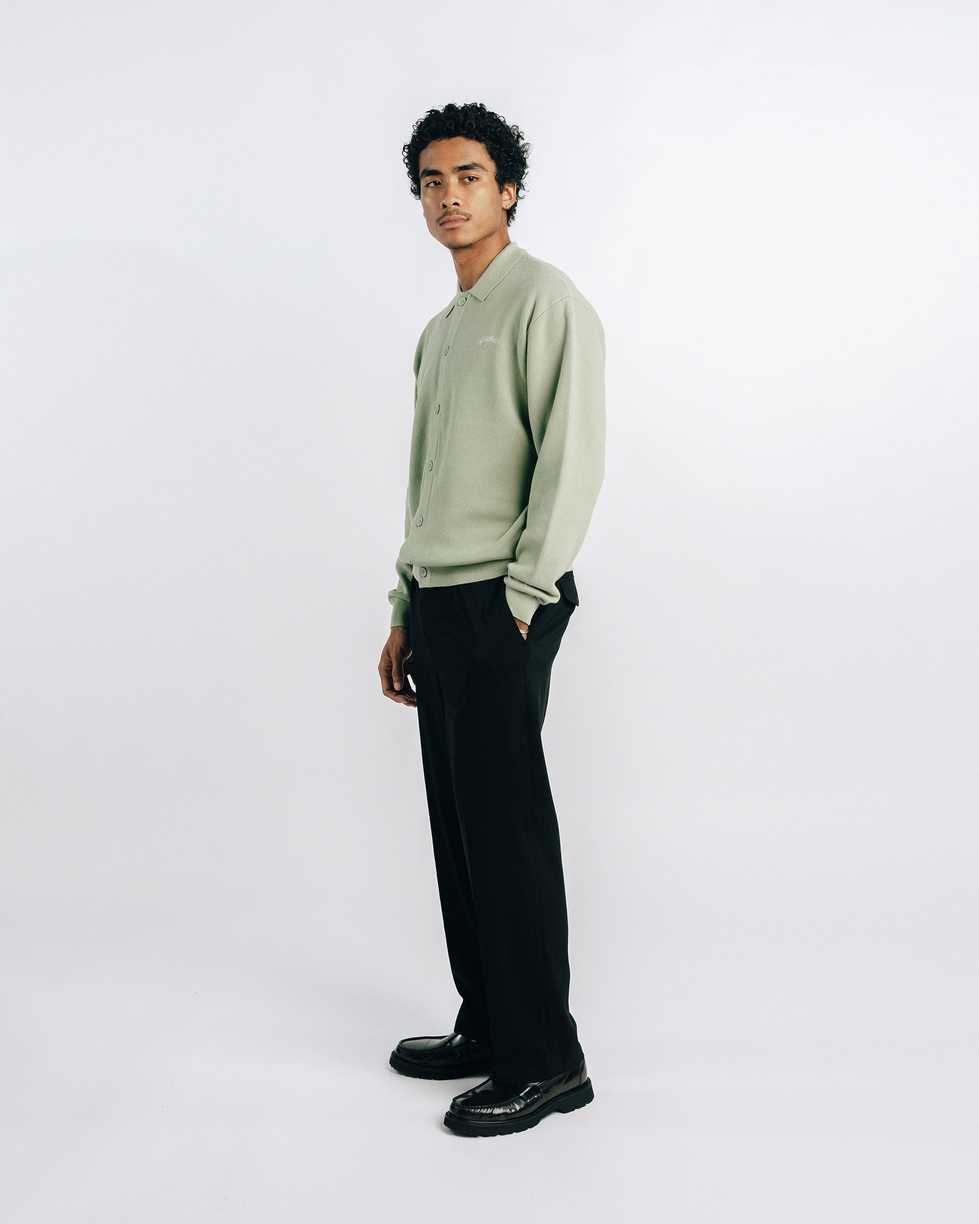 Man wearing a light green sweater and black pants on a white background