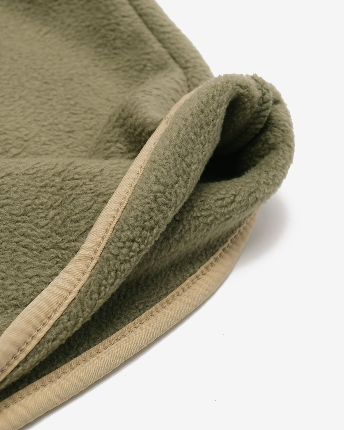 Close-up of a soft fleece garment or textile in muted olive green with a contrasting light beige stitched border, photographed on a clean white background.