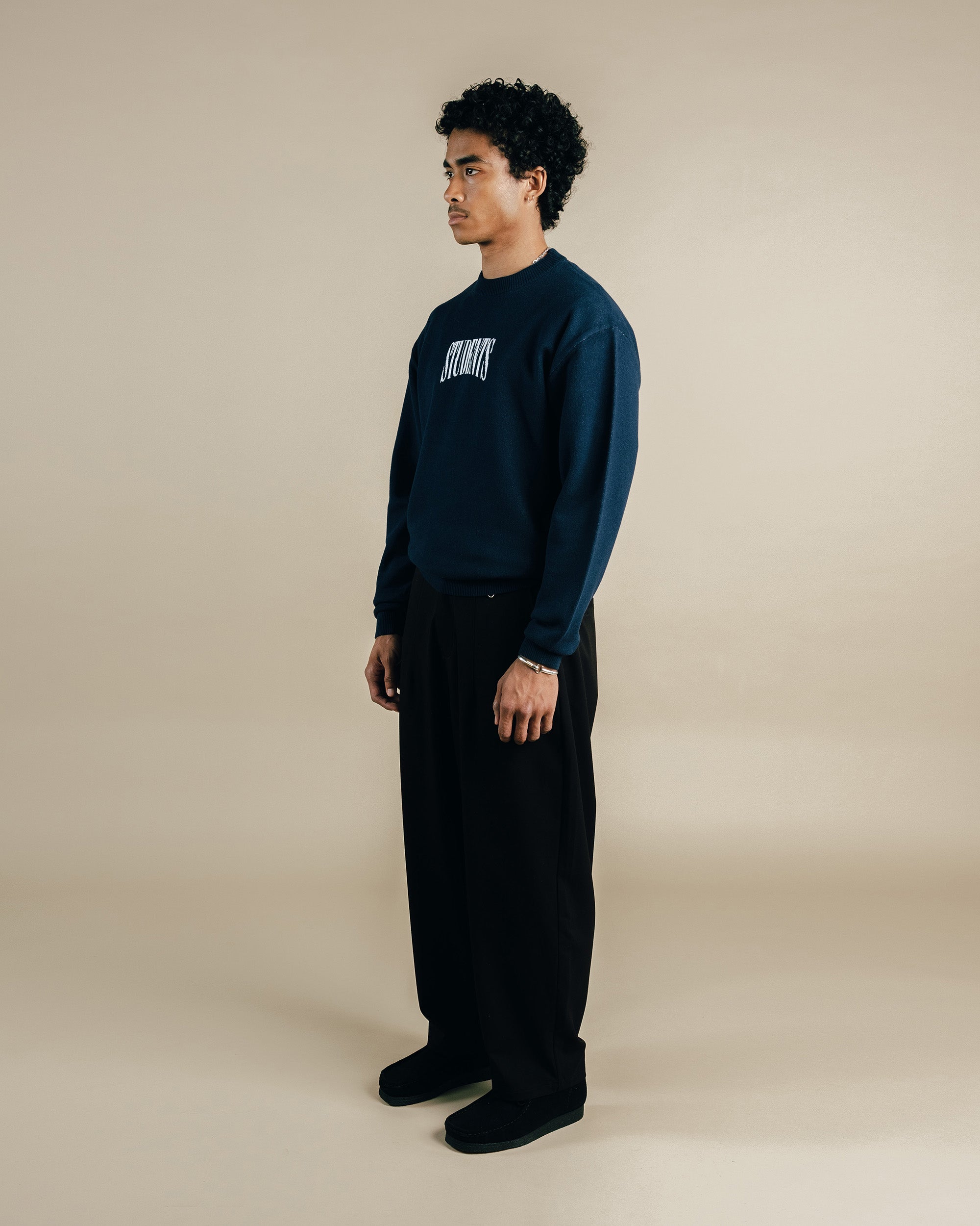 Person wearing a dark blue sweatshirt with text and black pants on a beige background