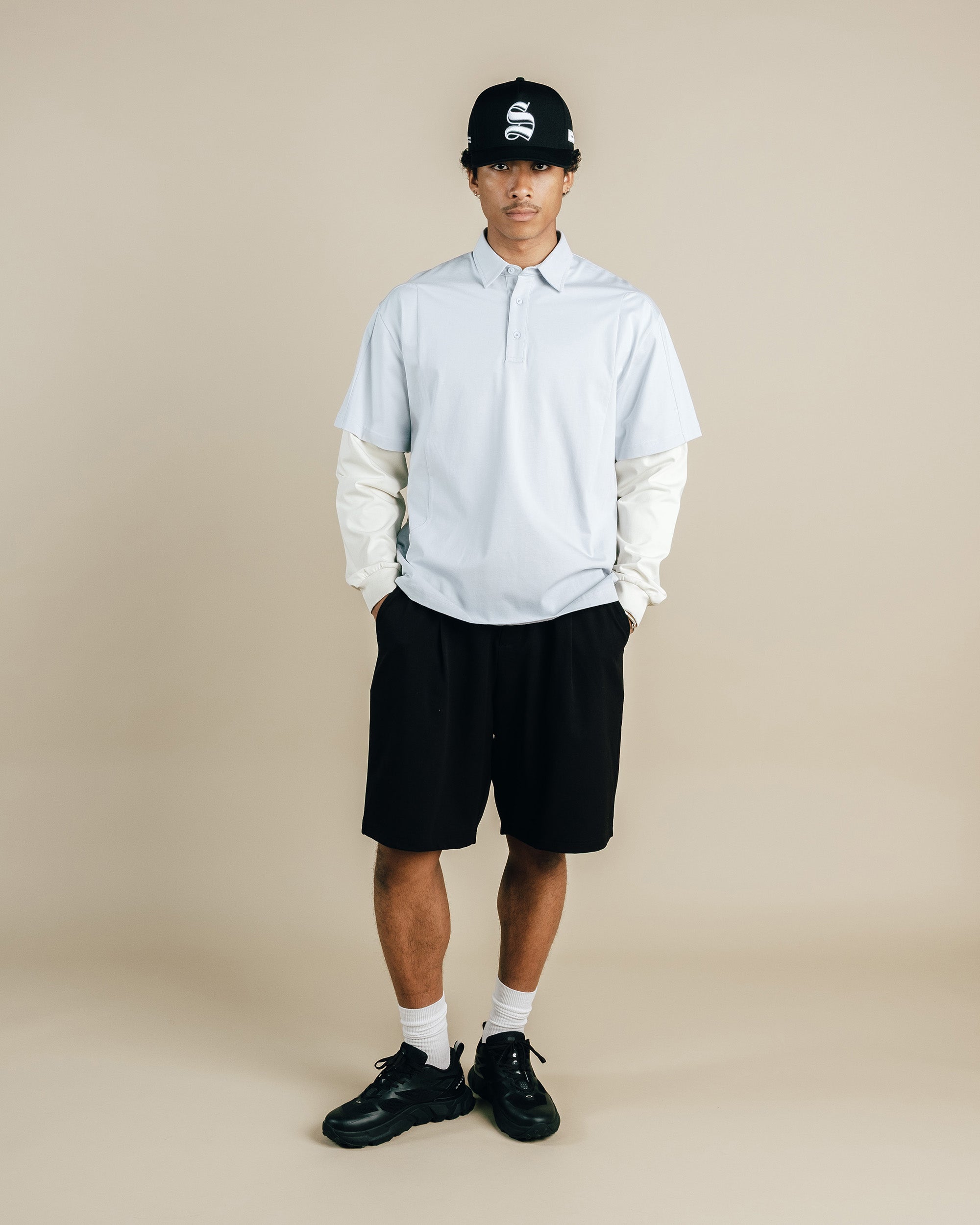 Person wearing a light gray hoodie with white sleeves, black shorts, and black shoes on a beige background