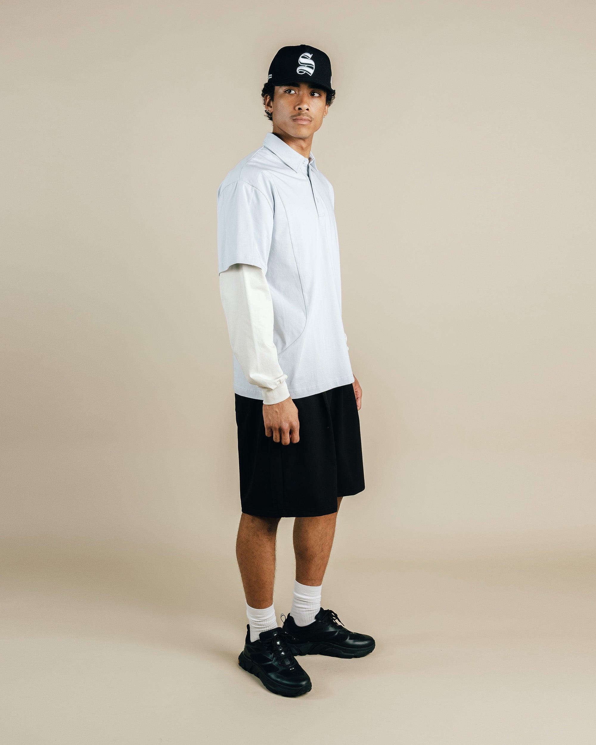 Person wearing a white shirt, black shorts, and black shoes on a beige background