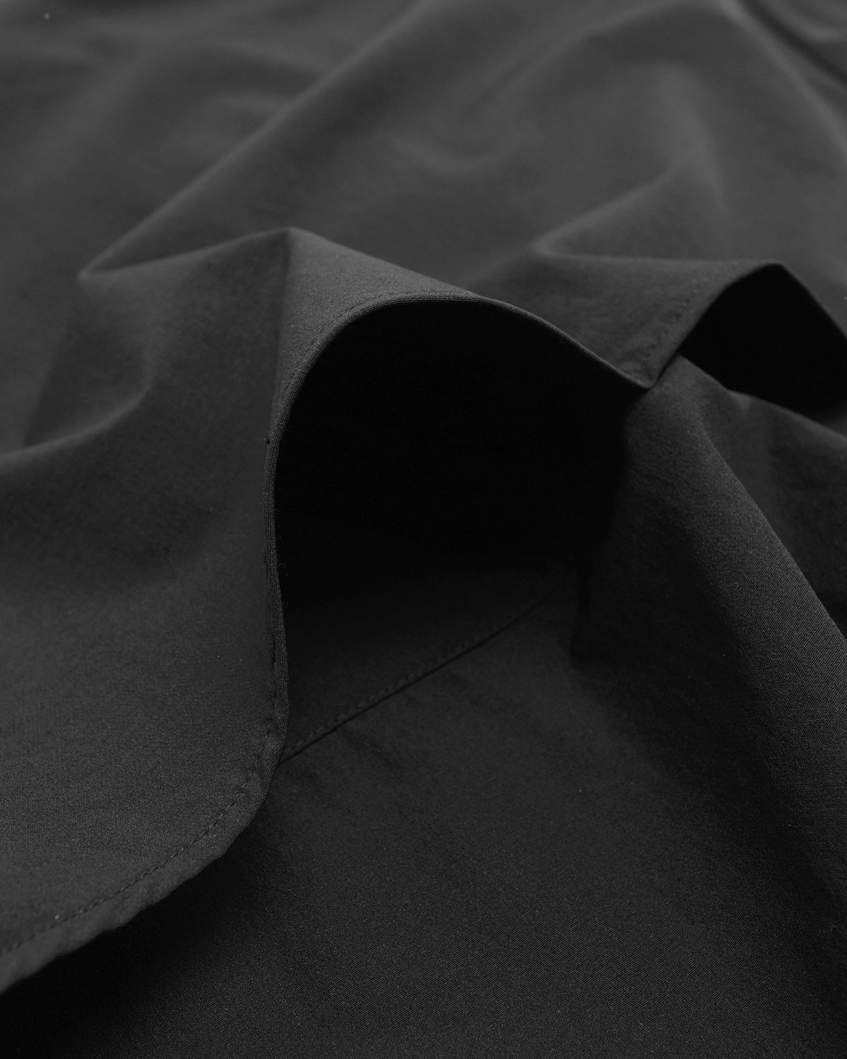 Close-up of a black fabric garment with soft folds and a stitched edge, shown in low light.
