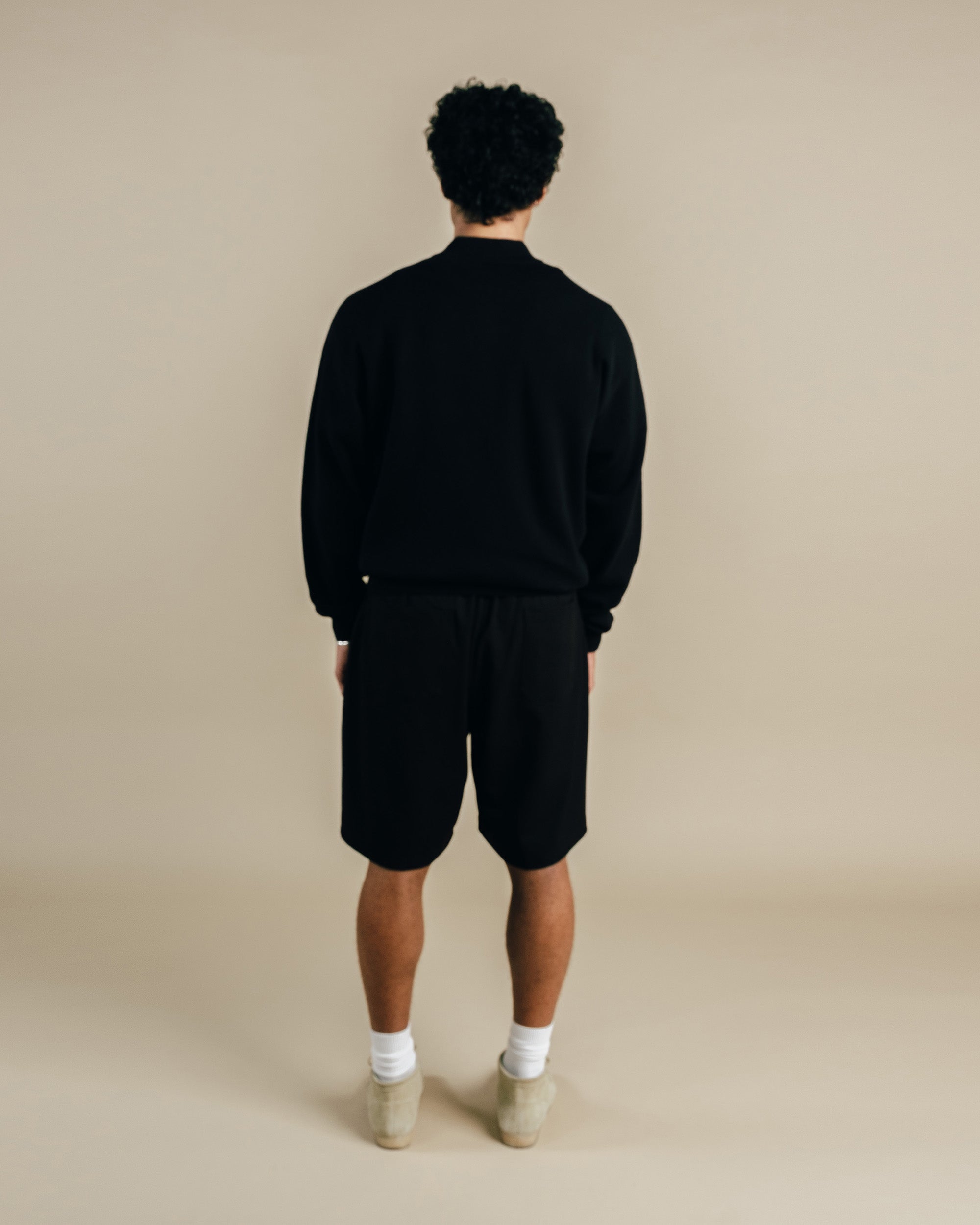 Person wearing a black tracksuit on a beige background