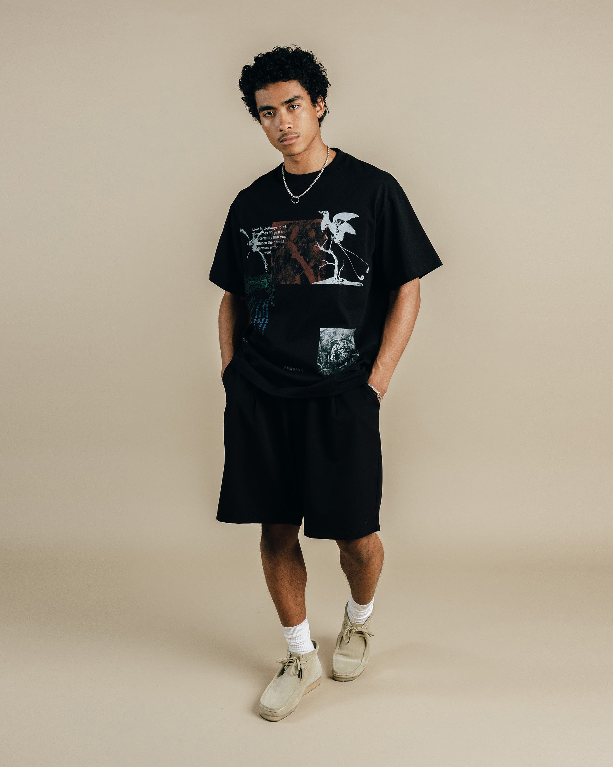 Person wearing a black graphic t-shirt and shorts on a beige background