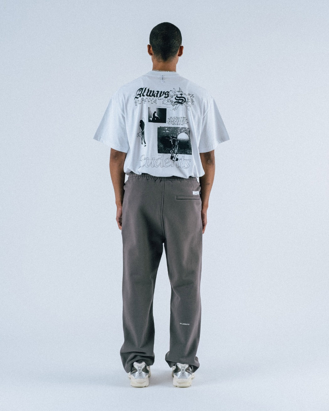 Person wearing a white t-shirt with graphic designs and gray pants on a light gray background