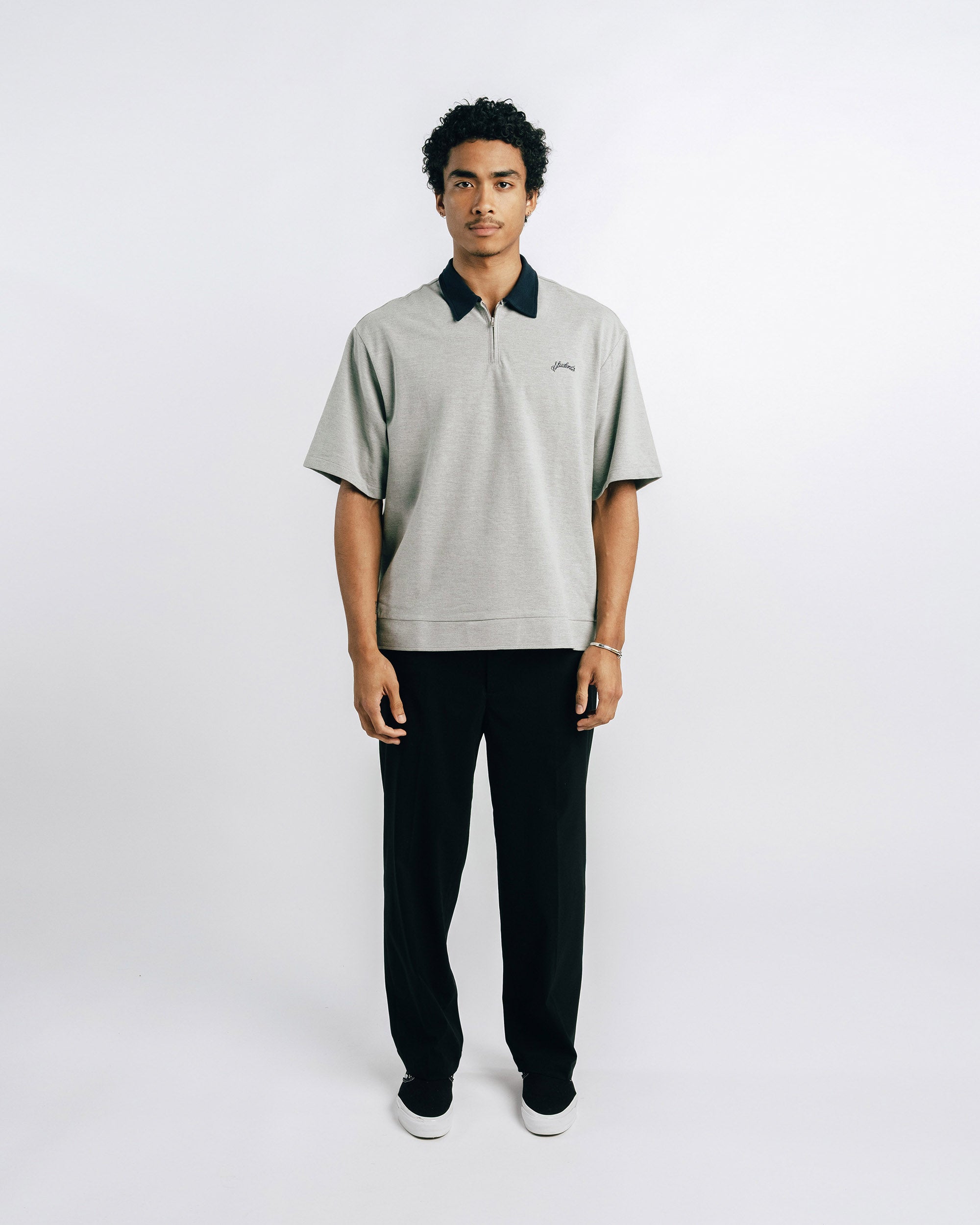 Person wearing a light gray polo shirt with black collar and trim, standing against a white background