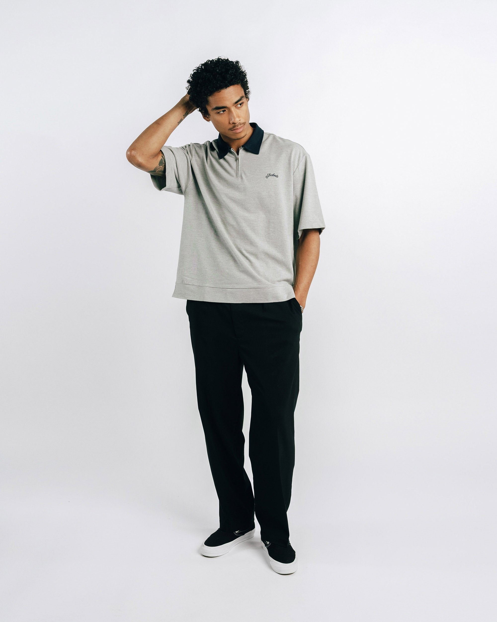 Person wearing a light gray polo shirt with black collar and trim, standing against a white background