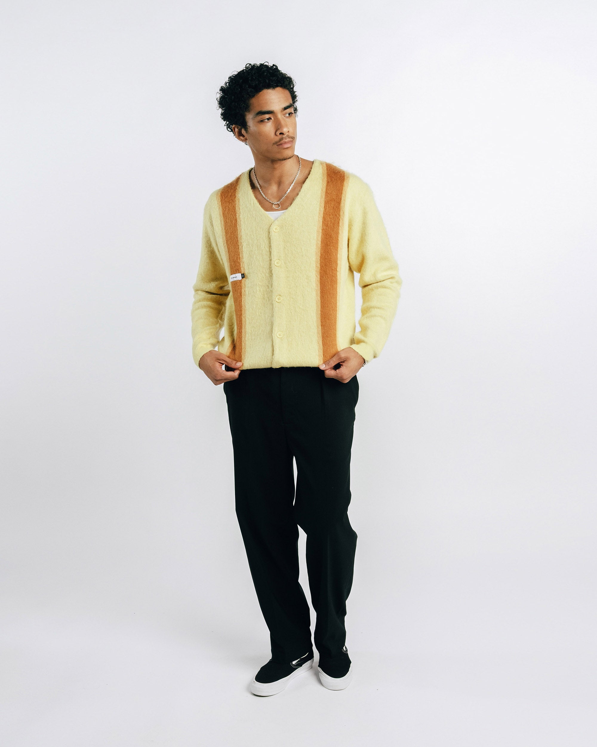 Man wearing a light yellow cardigan with brown stripes on a white background