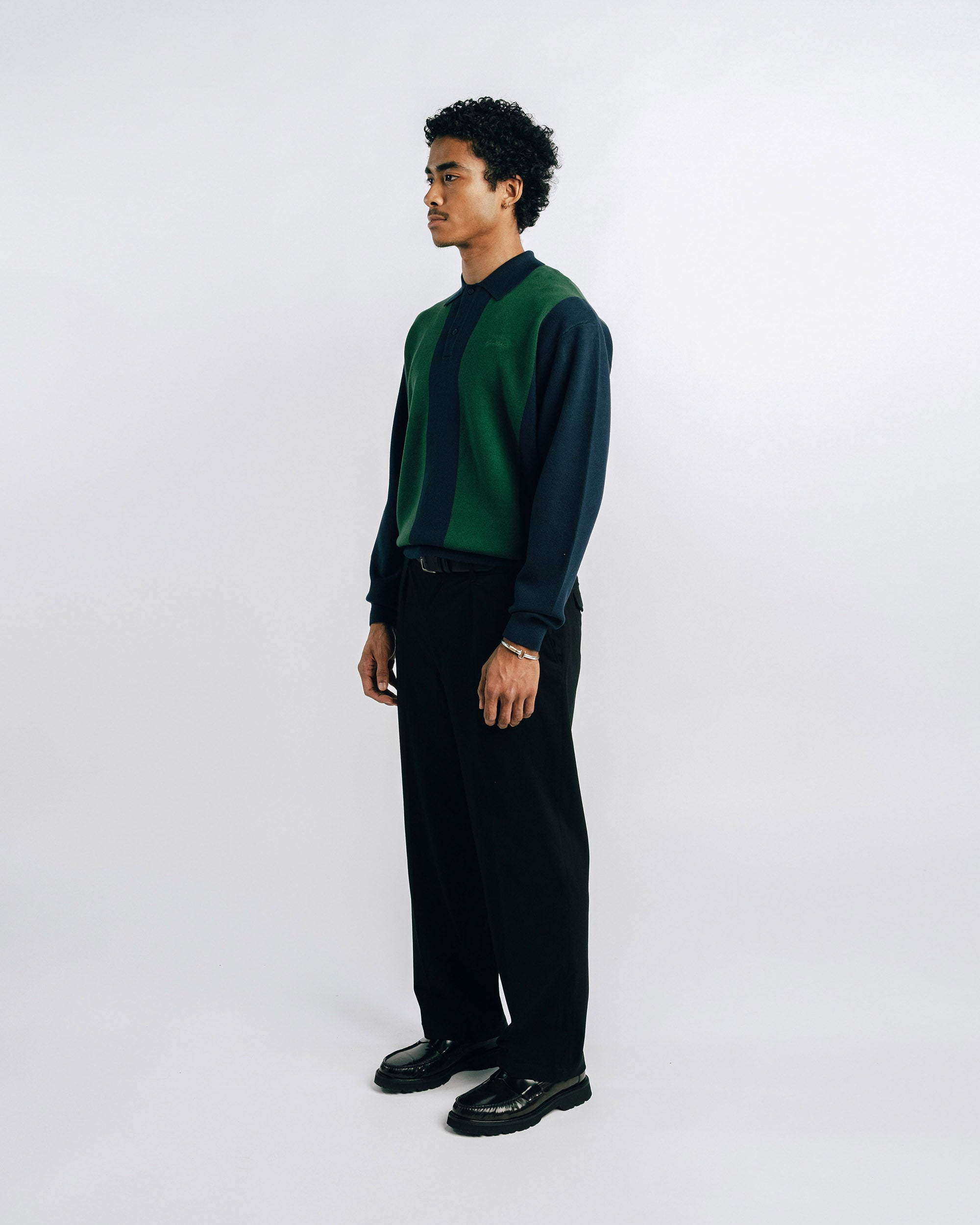 Man wearing a green and black shirt with black pants on a white 