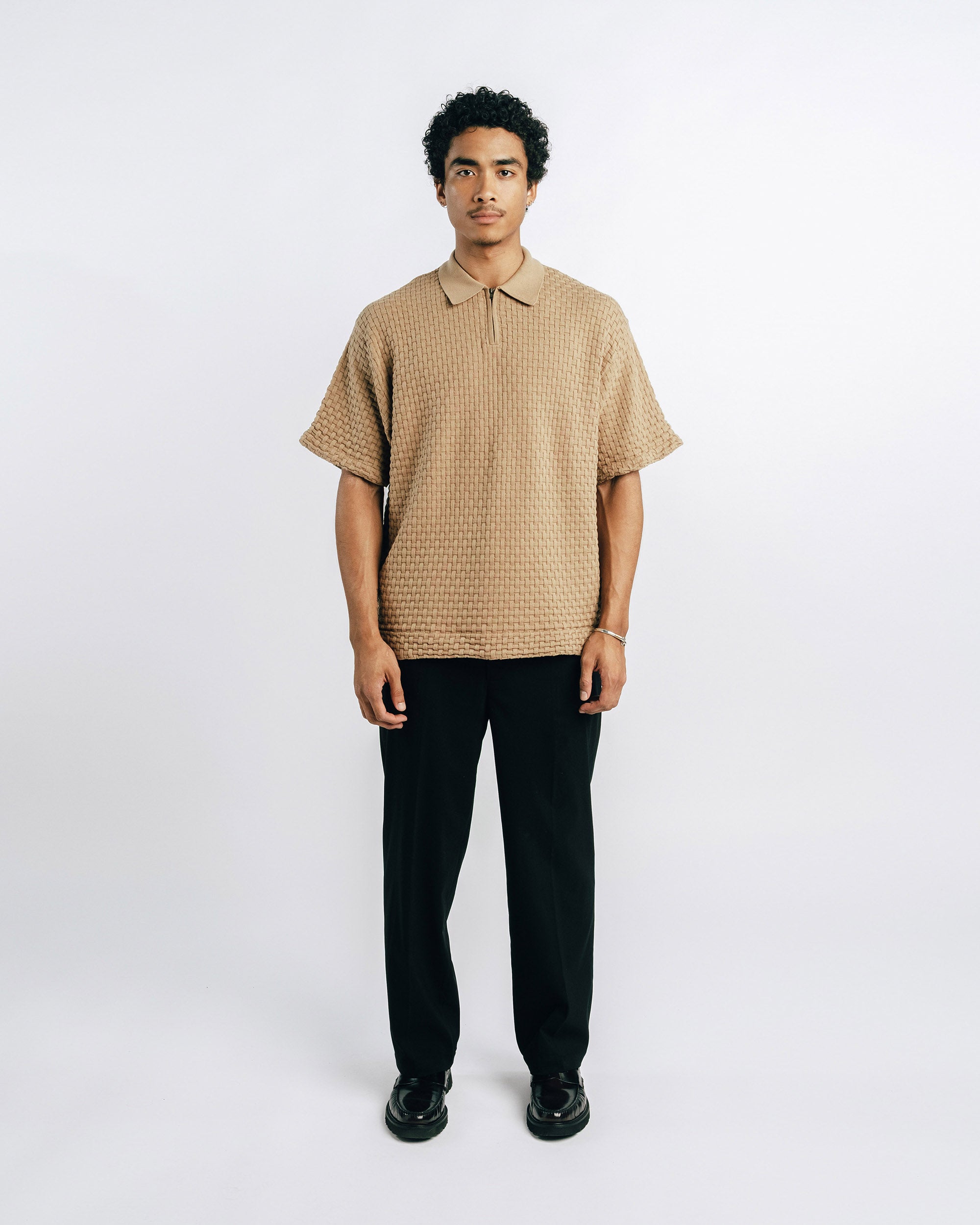 Man wearing a beige checkered shirt and black pants on a white background