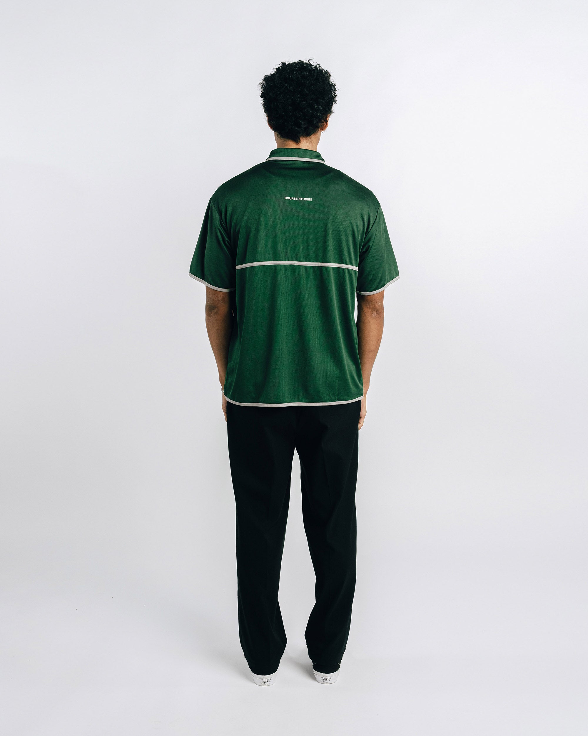 Person wearing a green polo shirt and black pants on a white background