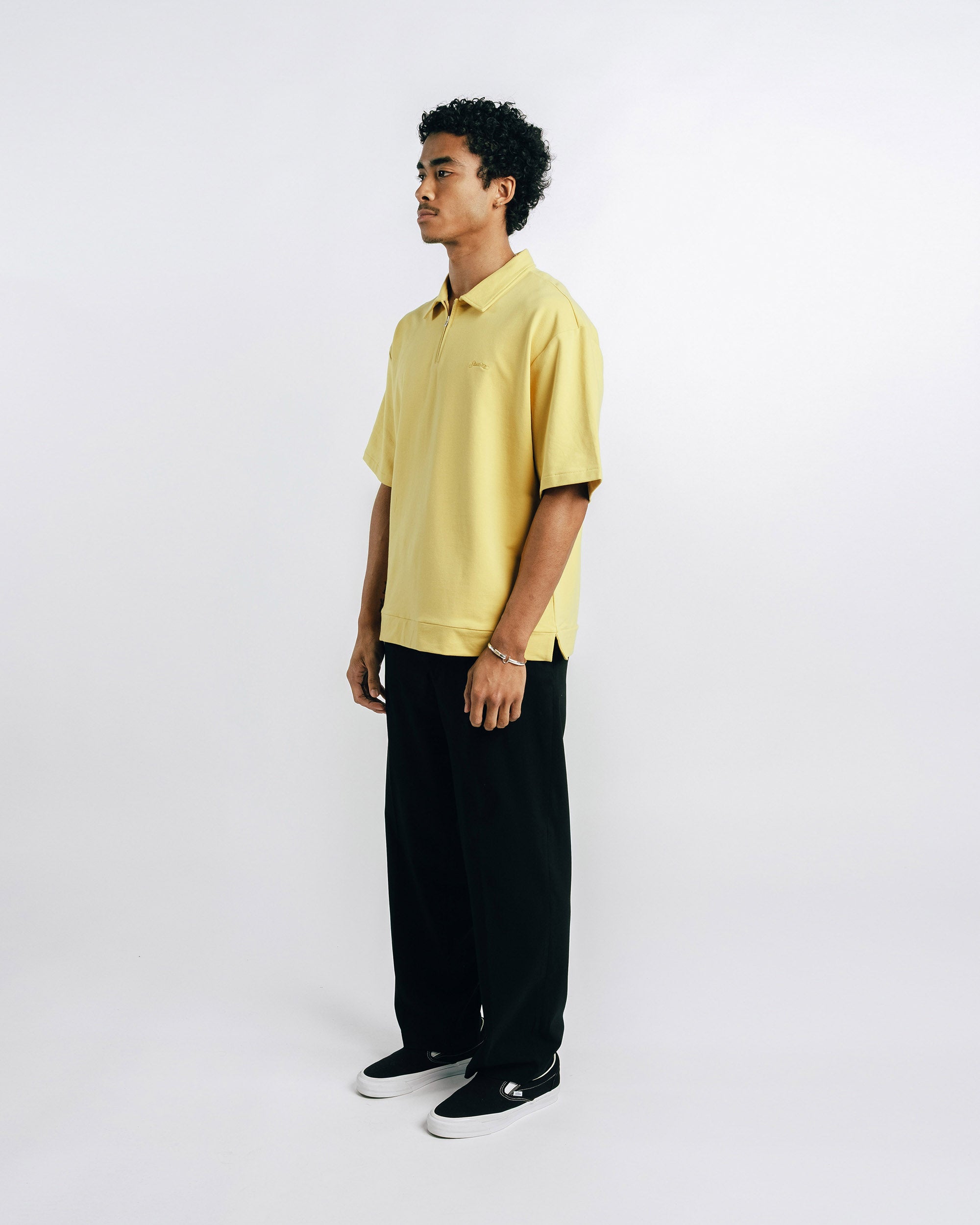 Person wearing a yellow polo shirt and black pants on a white background
