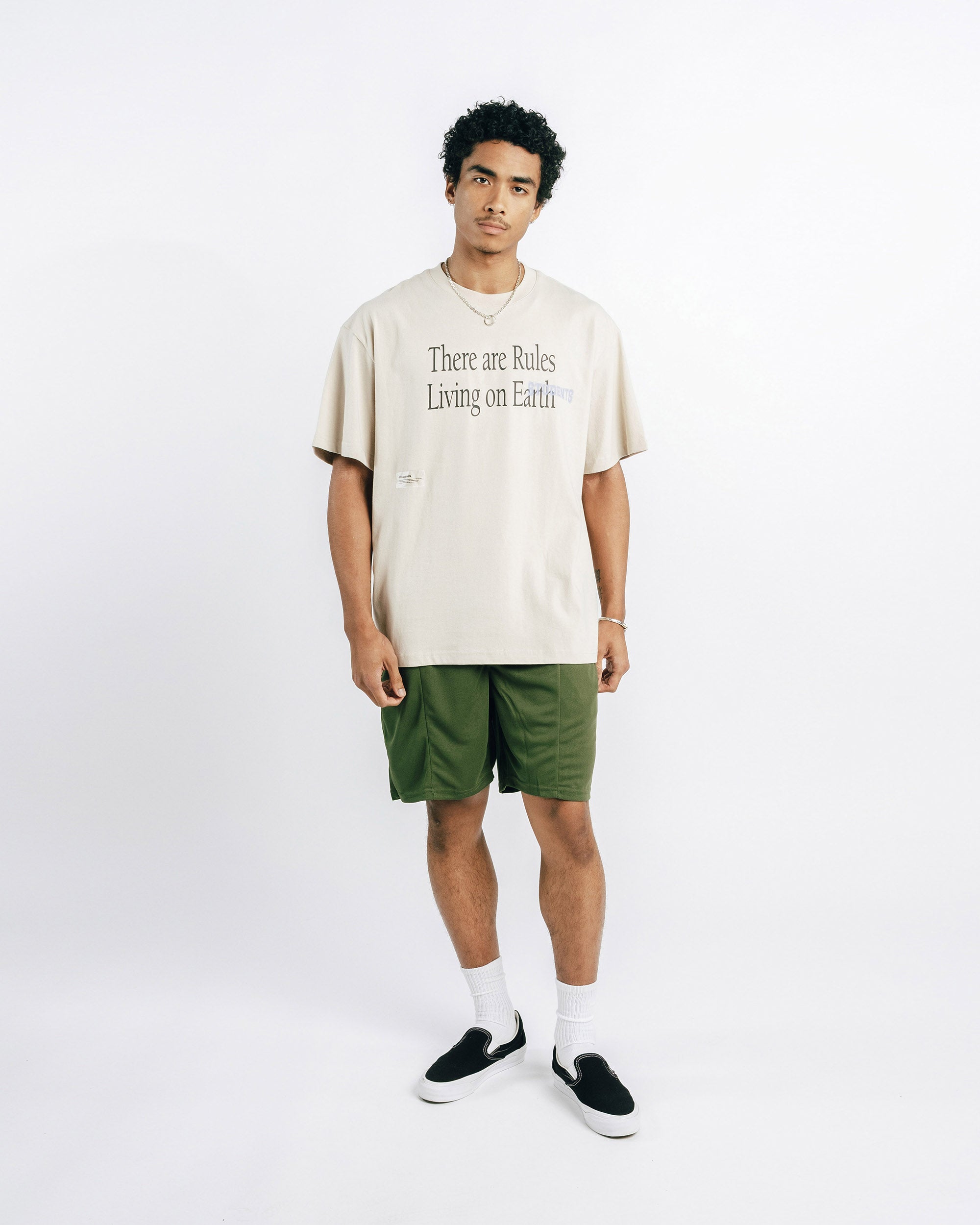 Man wearing a beige t-shirt with text and green shorts on a white background