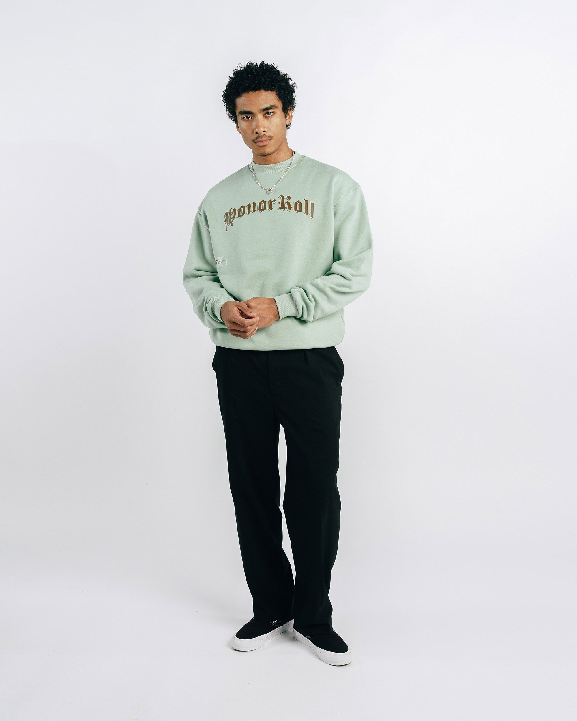 Person wearing a light green sweatshirt with text and black pants on a white background