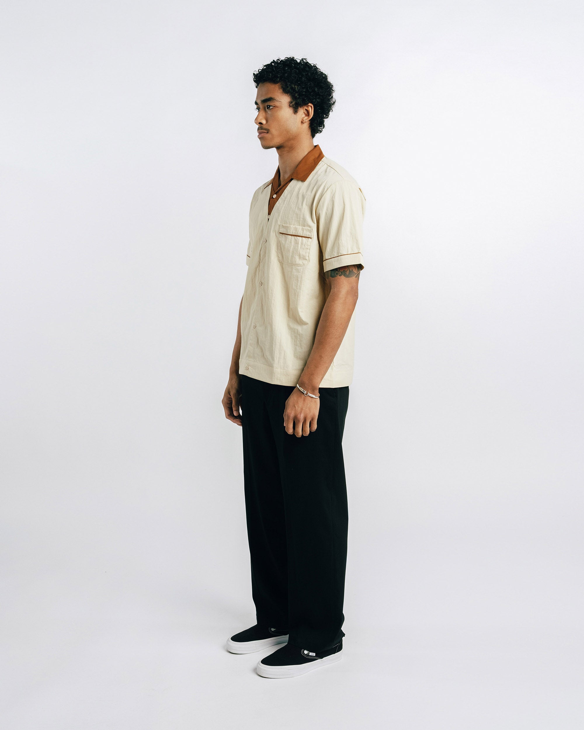Man wearing a beige shirt and black pants on a white background