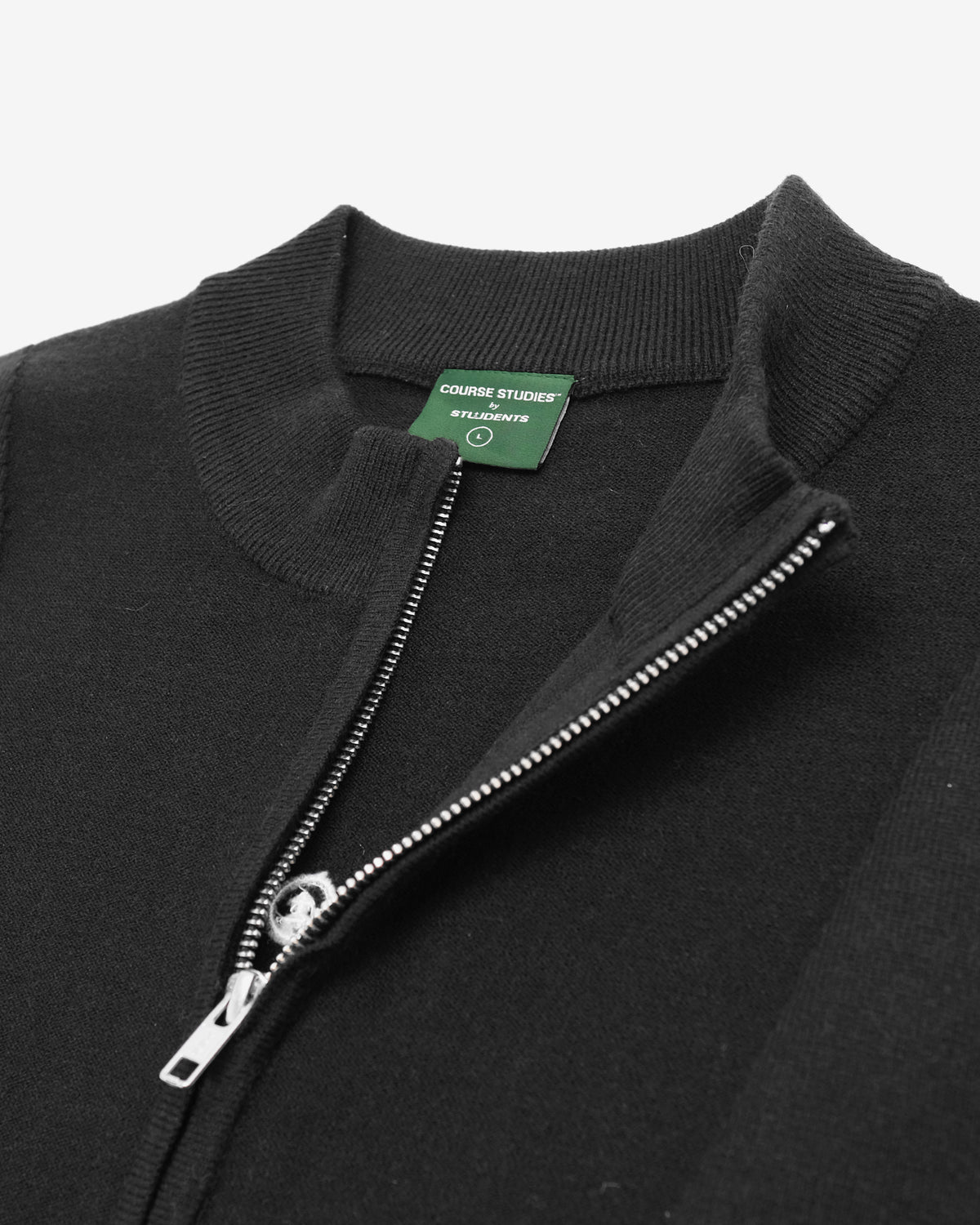Close-up of a black ribbed knit zip-up sweater with a silver zipper and a green neck label reading 'CROSBY SHOES'.