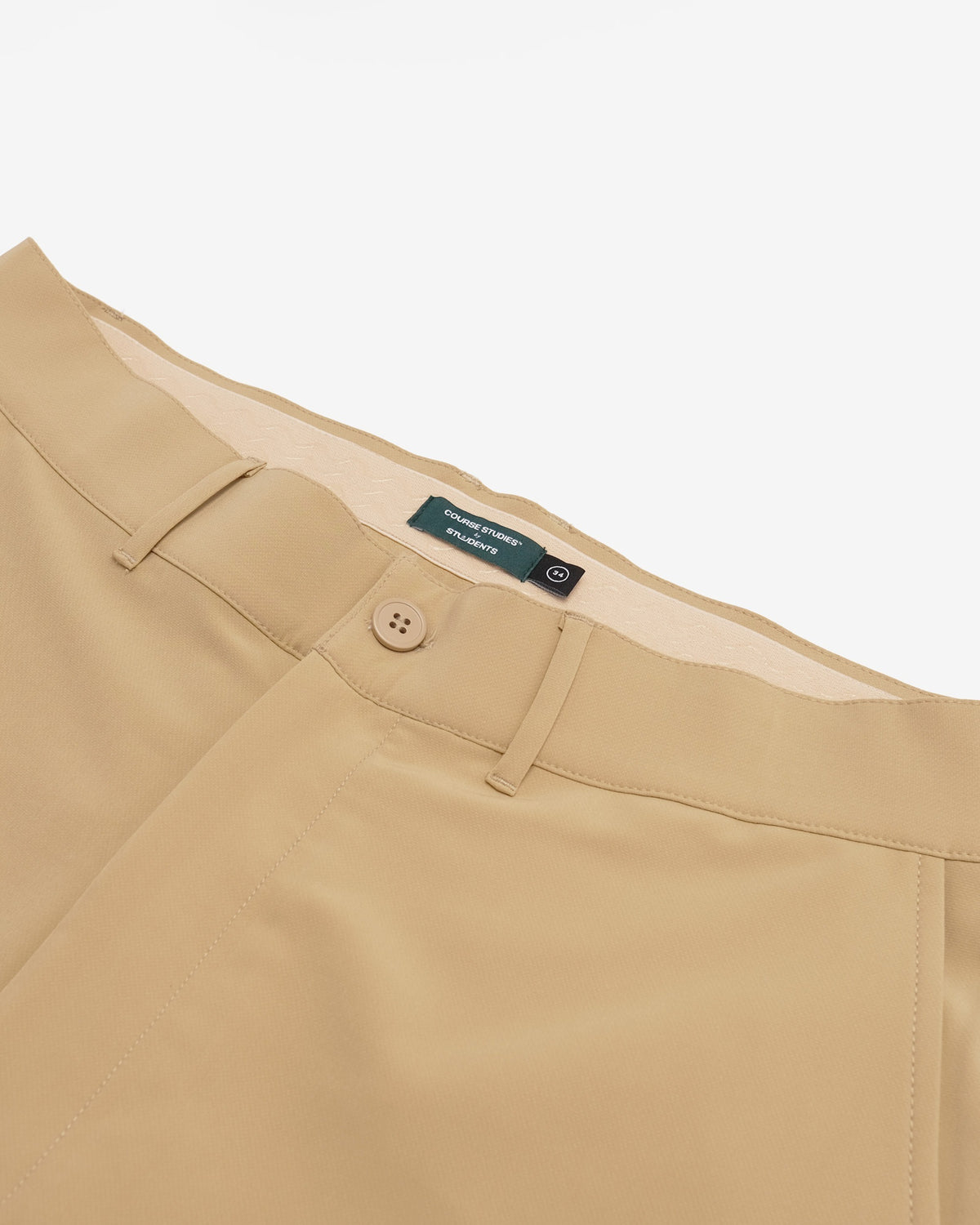 Close-up of tan chinos showing the waistband, belt loops, button closure, and a green brand label that reads 'The Normal Brand'.