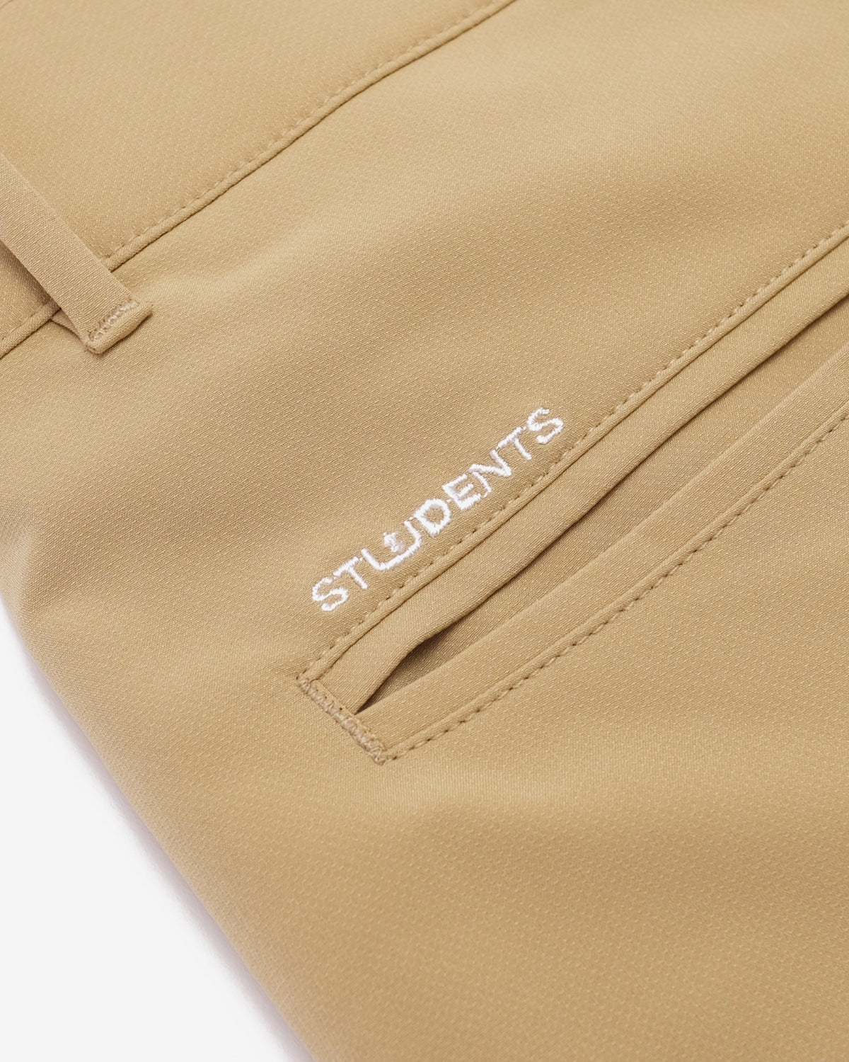 Close-up of a tan or khaki fabric garment, likely pants or a jacket, showing a pocket with the word STUDENTS embroidered in white on the side.