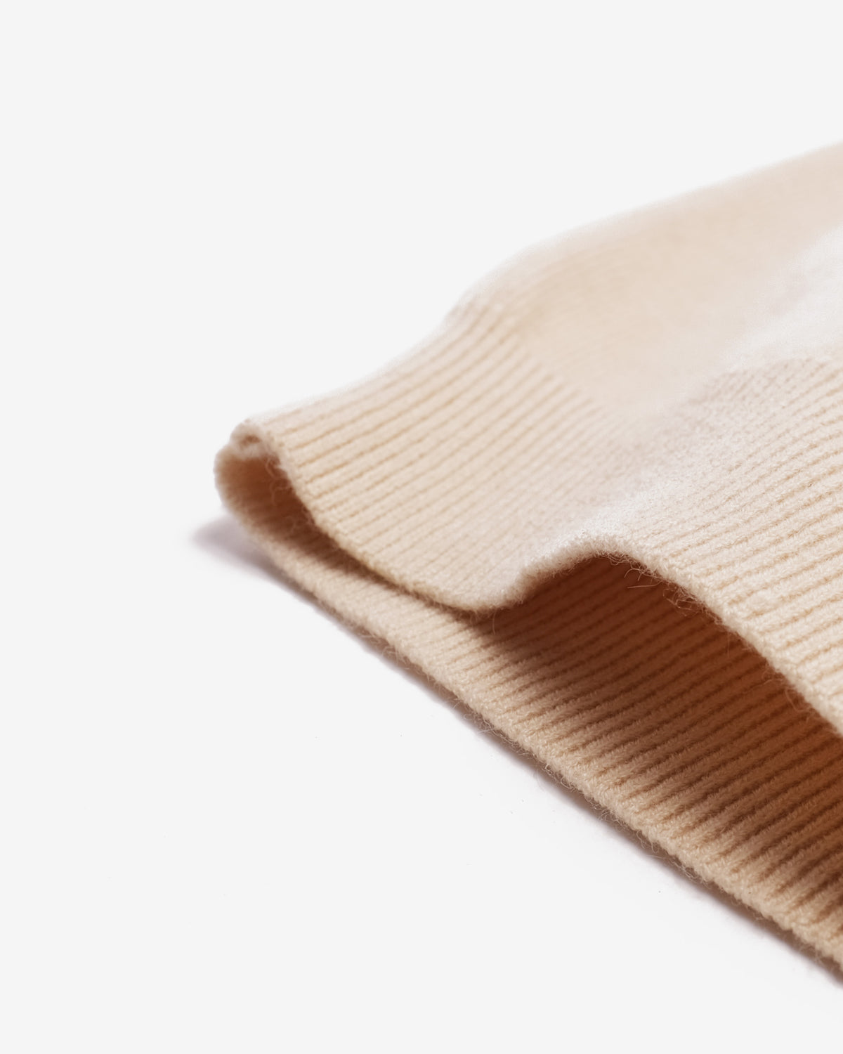 A close-up of a ribbed knit fabric cuff in a warm cream or light beige color, folded to show the texture and ribbed edge against a plain white background.