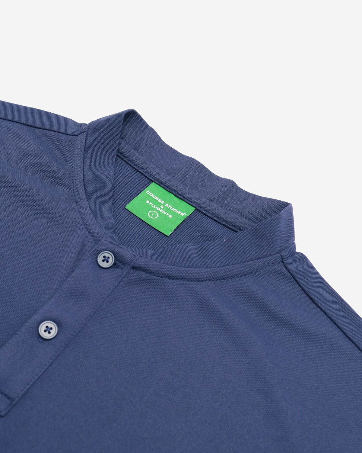 Close-up of a navy blue polo shirt showing the collar, a green inner neck label, and the top of a buttoned placket on a light gray background.