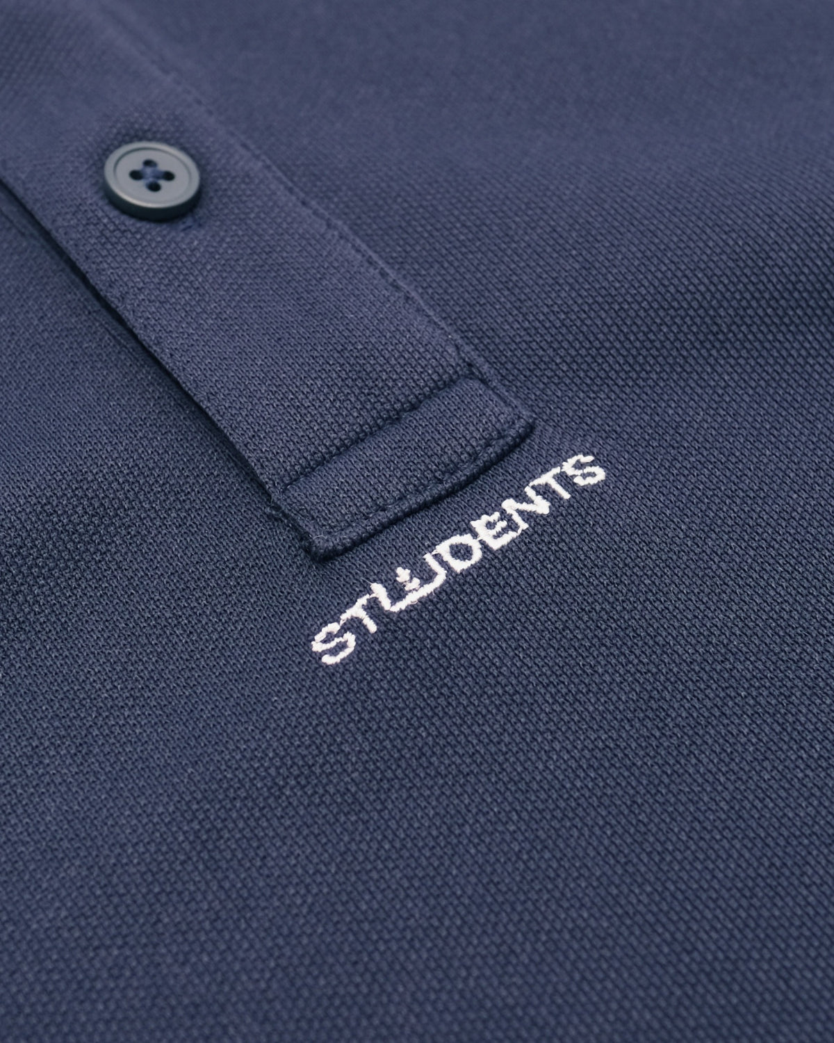 Close-up of a navy blue textured polo shirt with a white embroidered 'STUDENTS' logo on the chest and a matching navy button on the collar.