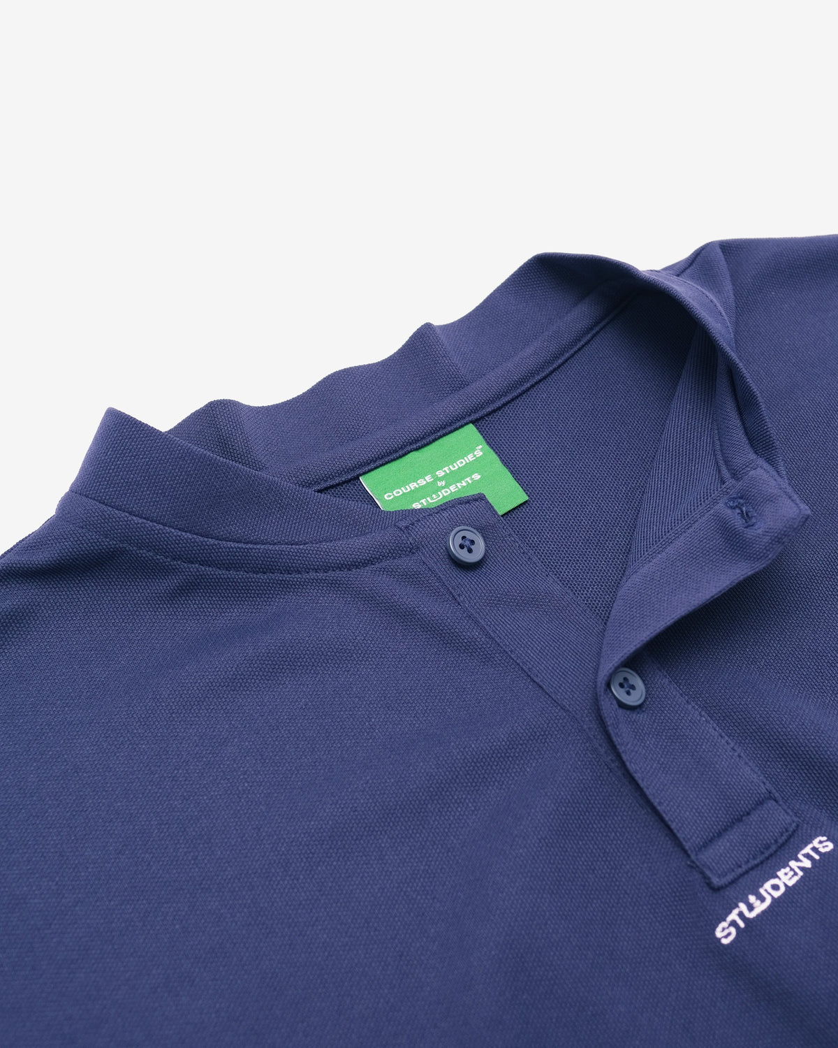 Close-up of a navy blue polo shirt with a green brand label and white 'STUDENTS' text on the chest pocket.