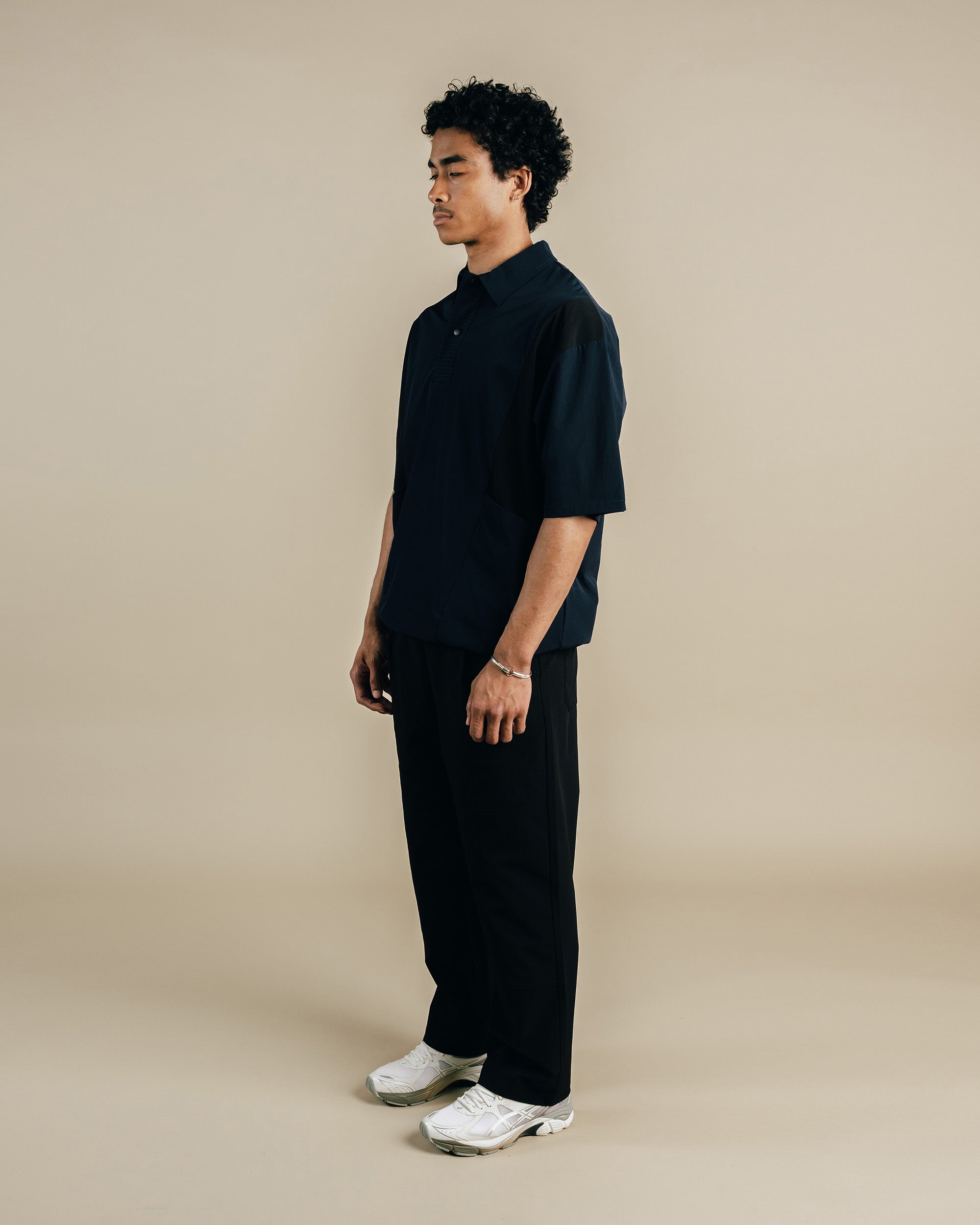 Man wearing a black outfit with white sneakers on a beige background